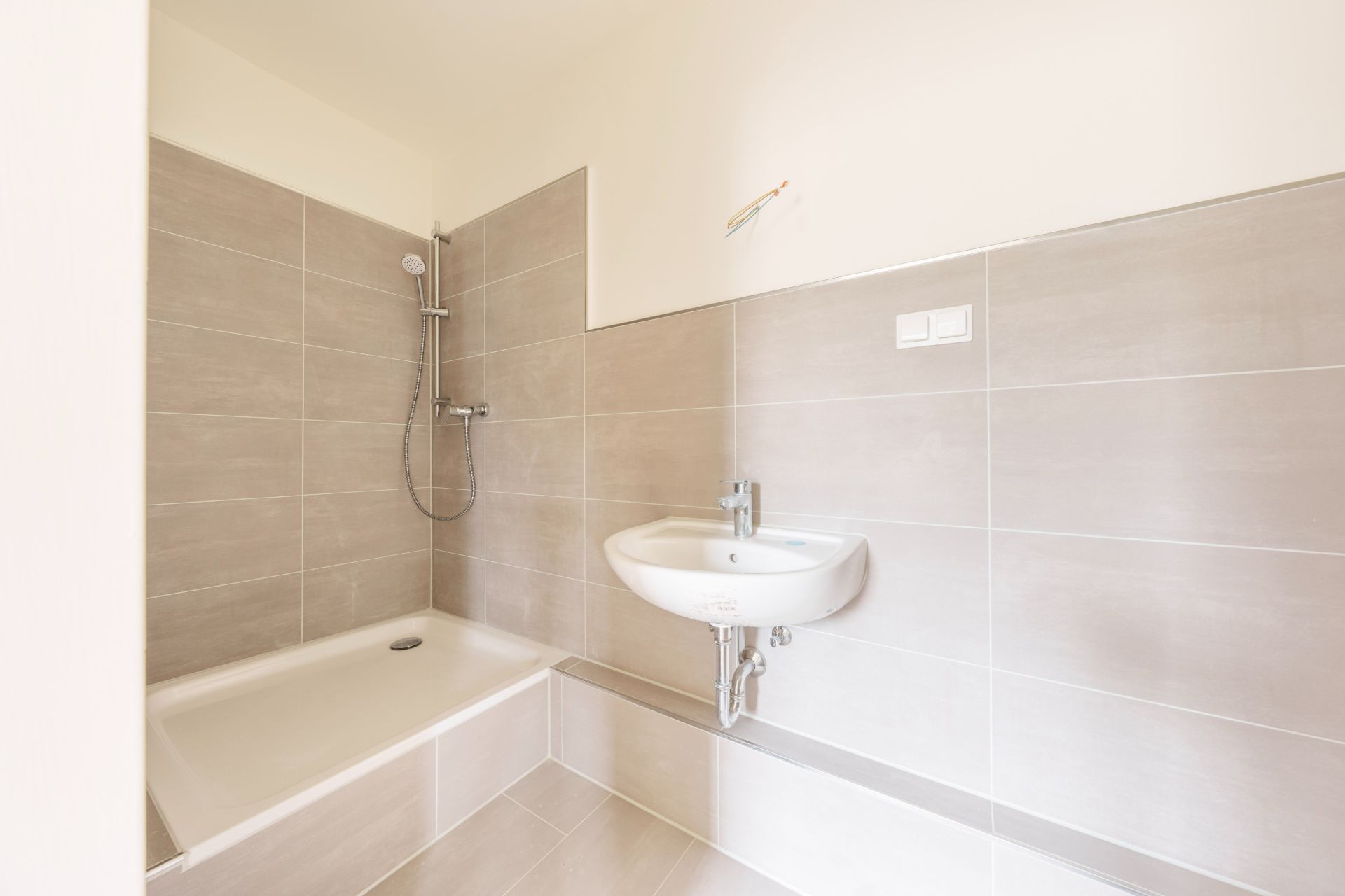 Modernes Badezimmer mit Dusche, Waschbecken und beigen Fliesen an Wand und Boden.