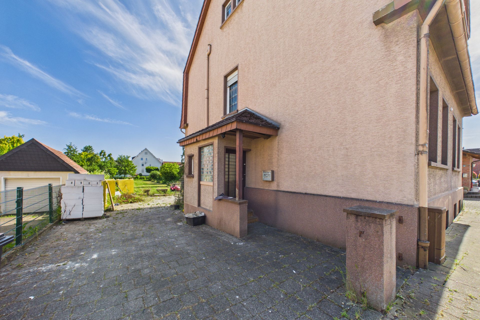Eingangsbereich eines Wohnhauses mit gepflastertem Hof und Garten im Hintergrund.