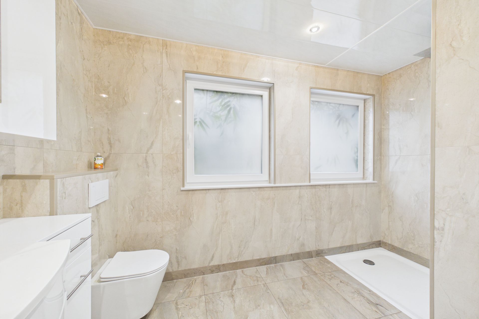 Modernes Badezimmer mit zwei Fenstern, einer Toilette und einer offenen Dusche auf Fliesenboden.