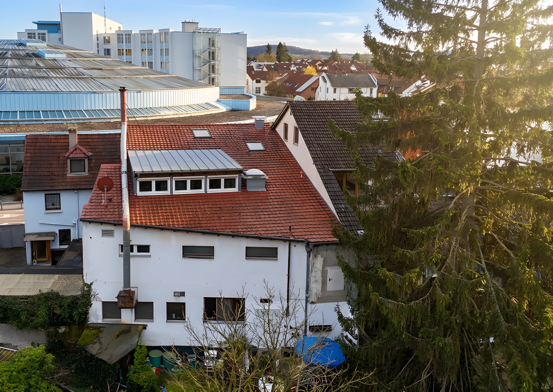 Wohnhaus mit rotem Dach und mehreren Fenstern, große Tanne im Vordergrund.