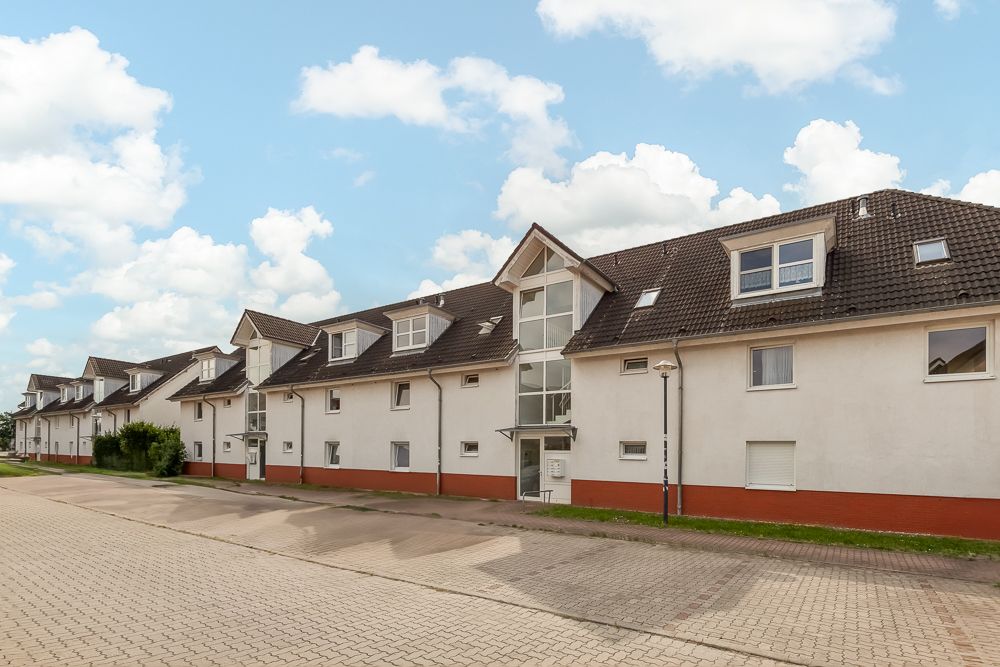 Mehrfamilienhaus mit weißer Fassade und rotem Sockel an einer gepflasterten Straße.