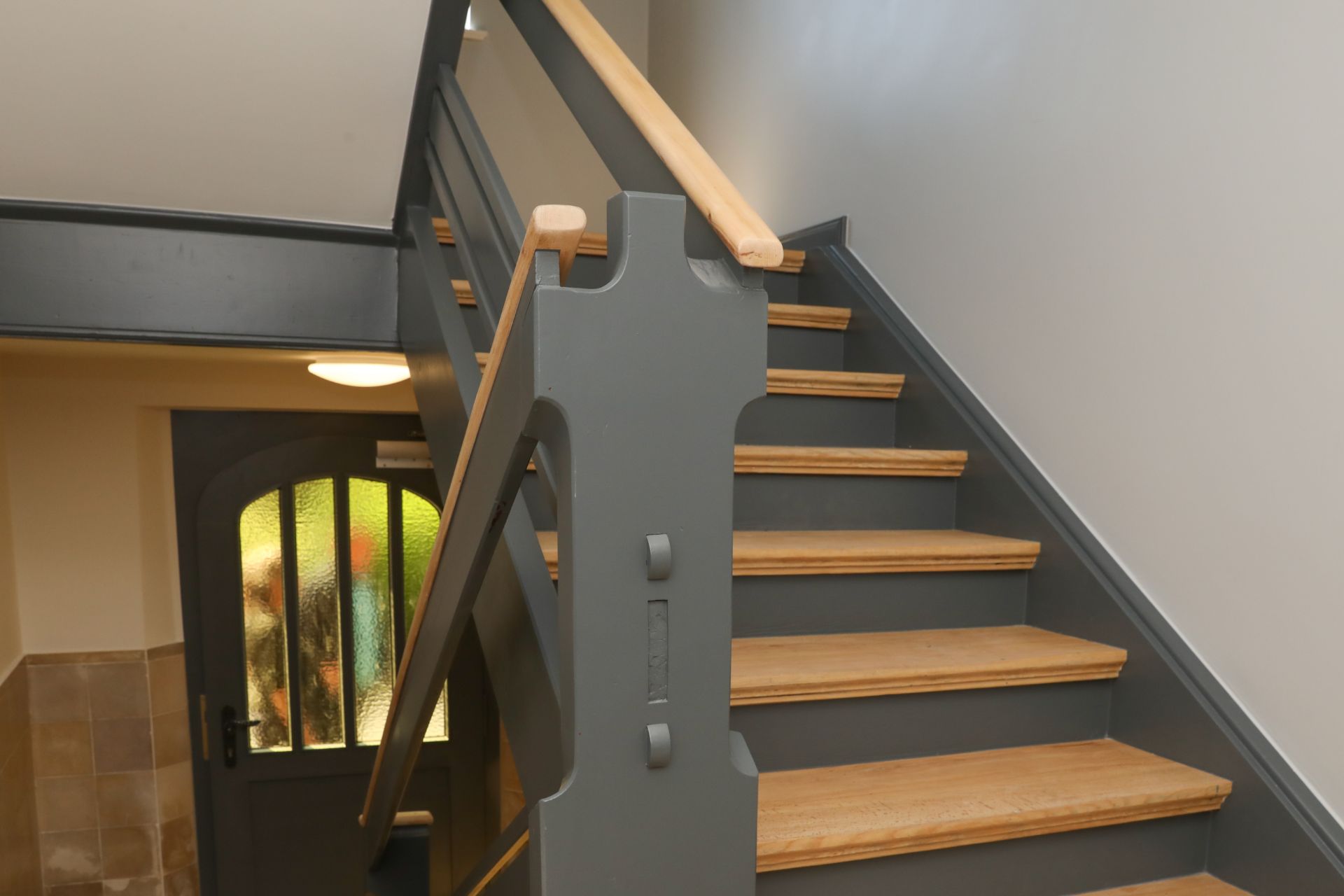 Holztreppe mit grauem Geländer in einem Wohnhausflur.