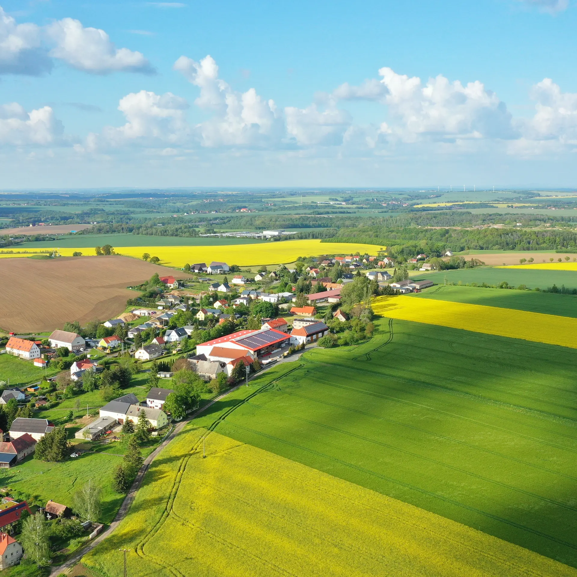 Luftaufnahme eines kleinen Dorfes mit umliegenden Feldern und Häusern bei Tageslicht.