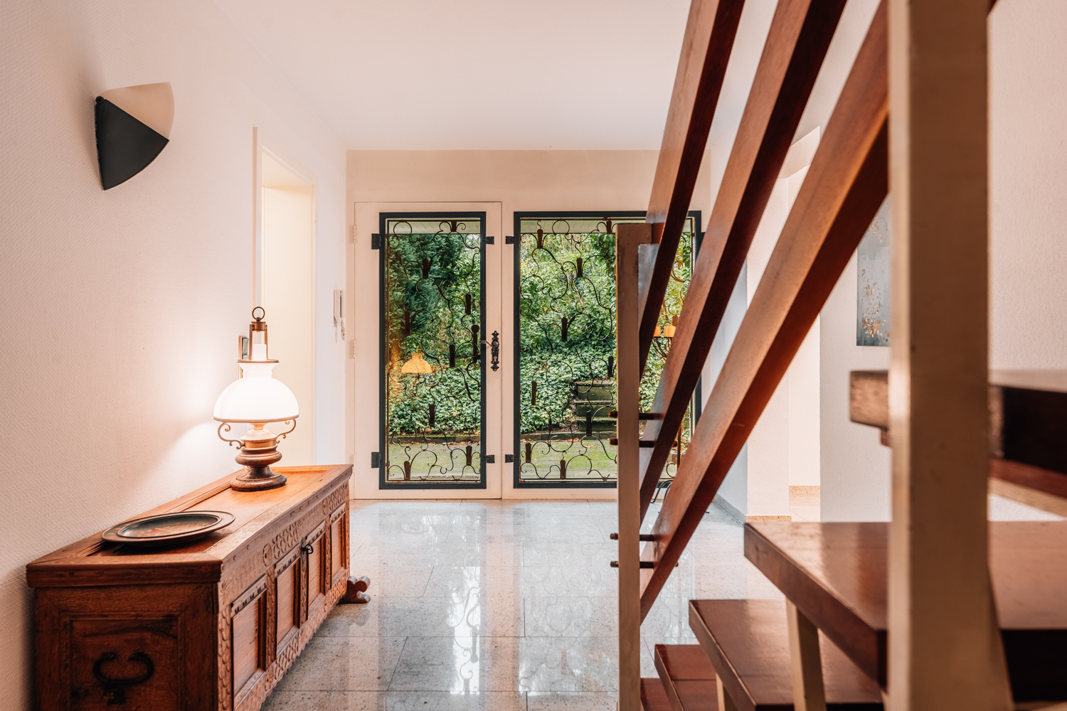 Heller Flur mit Holztreppe, Kommode und Glastüren zum Garten.