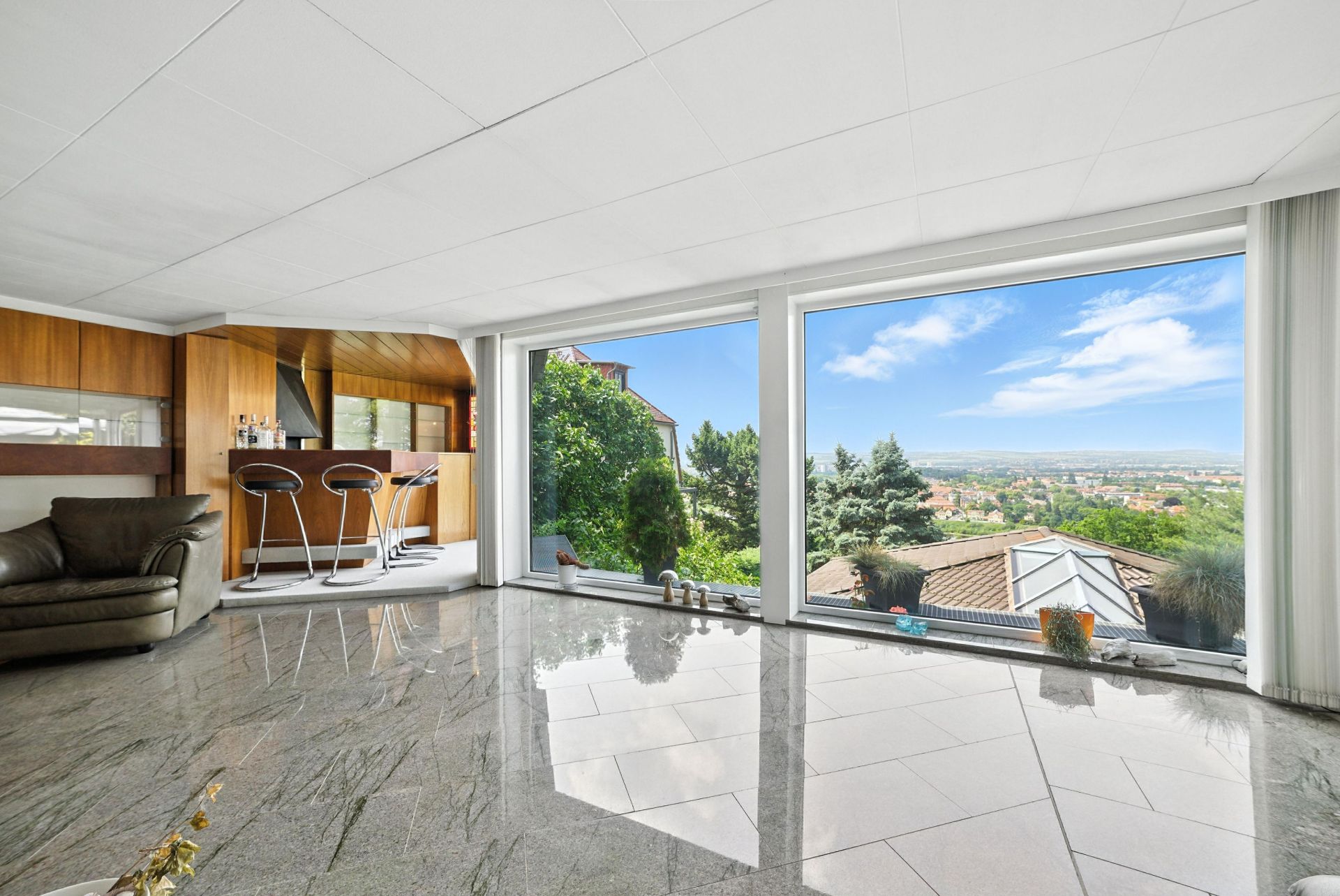 Modernes Wohnzimmer mit großen Fenstern, Marmorboden und Blick auf Garten und Stadt.