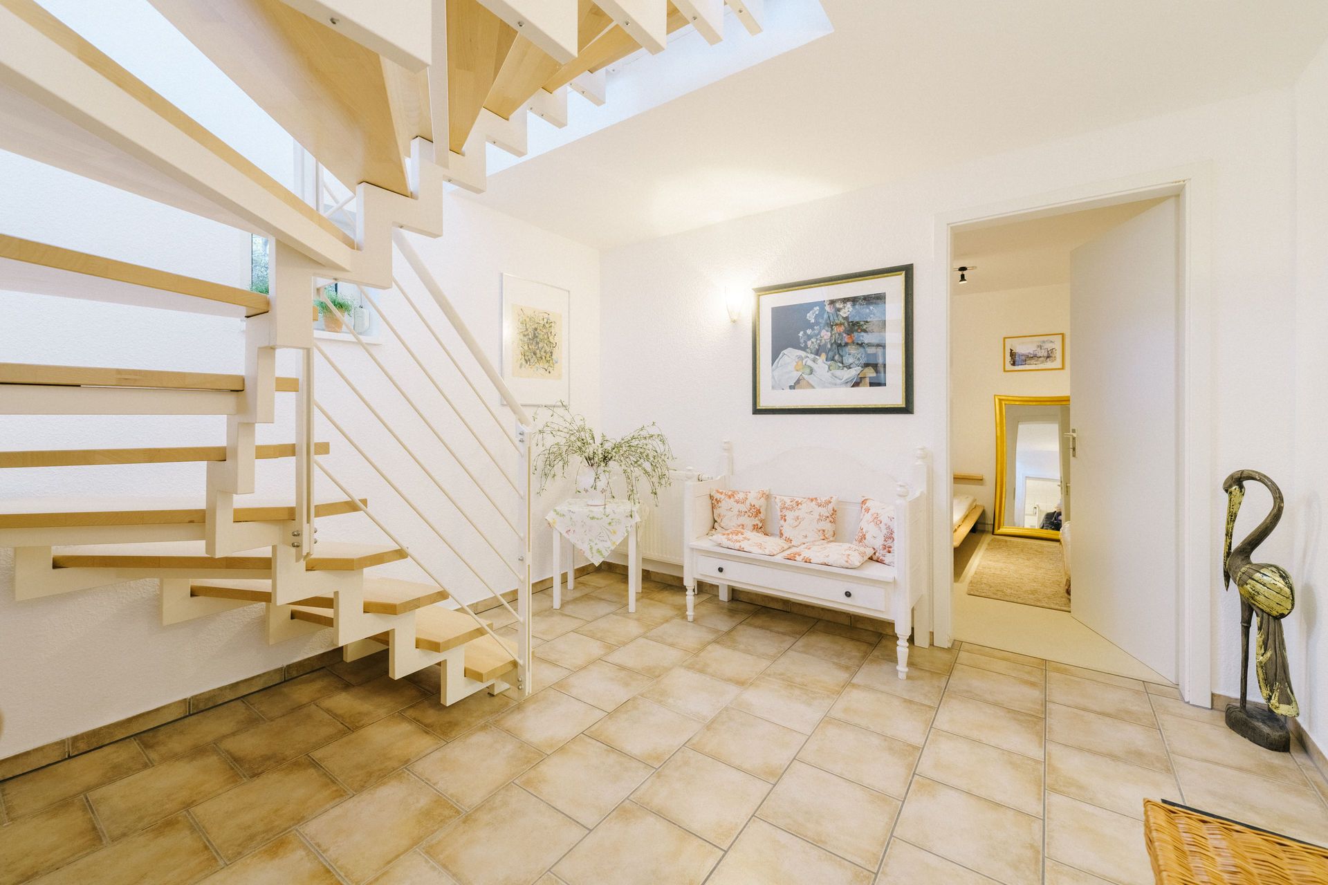 Heller Flur mit offener Treppe, Sitzbank, Wandbildern und gefliestem Boden.