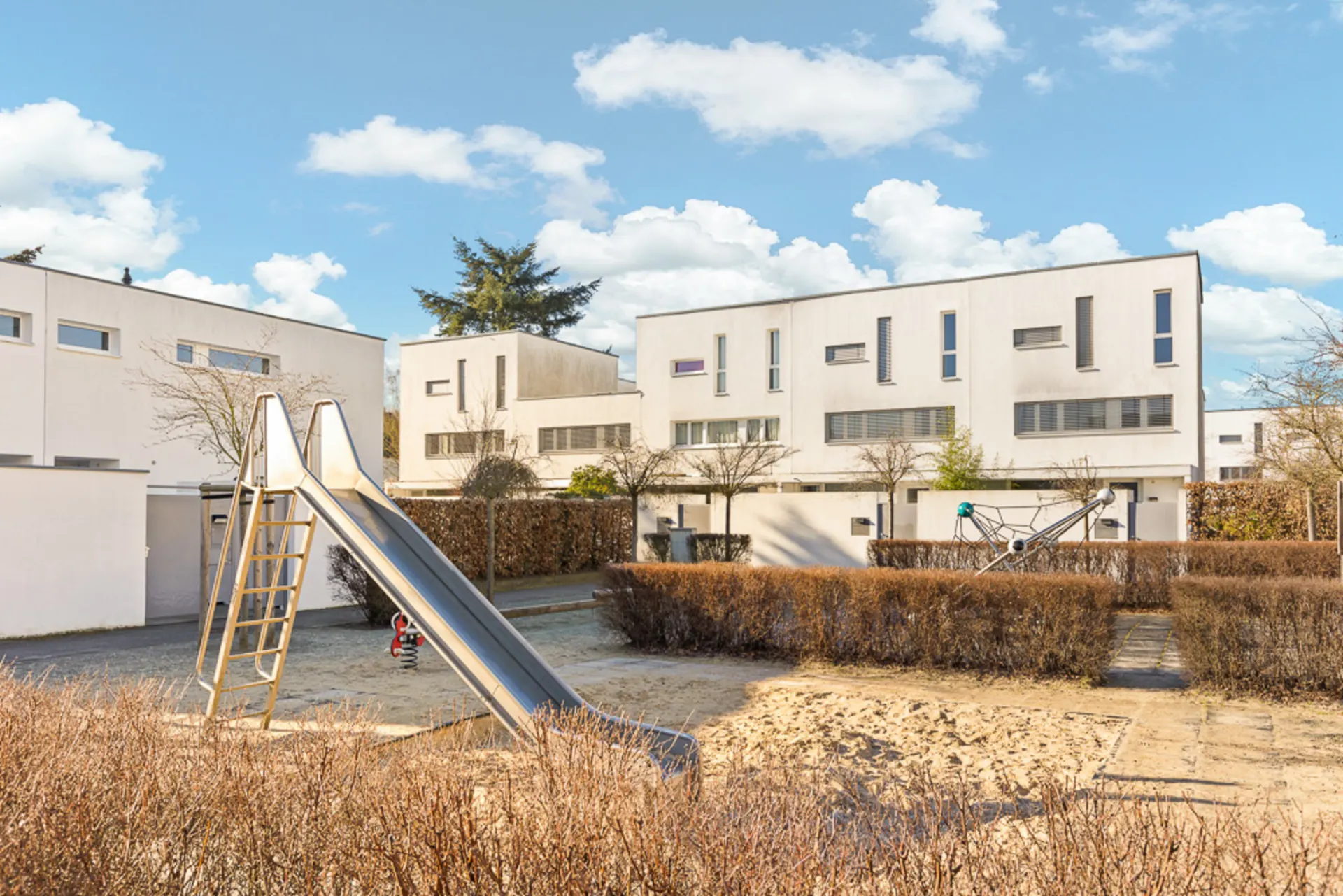 Spielplatz mit Rutsche und Klettergerüst vor modernen weißen Wohnhäusern.