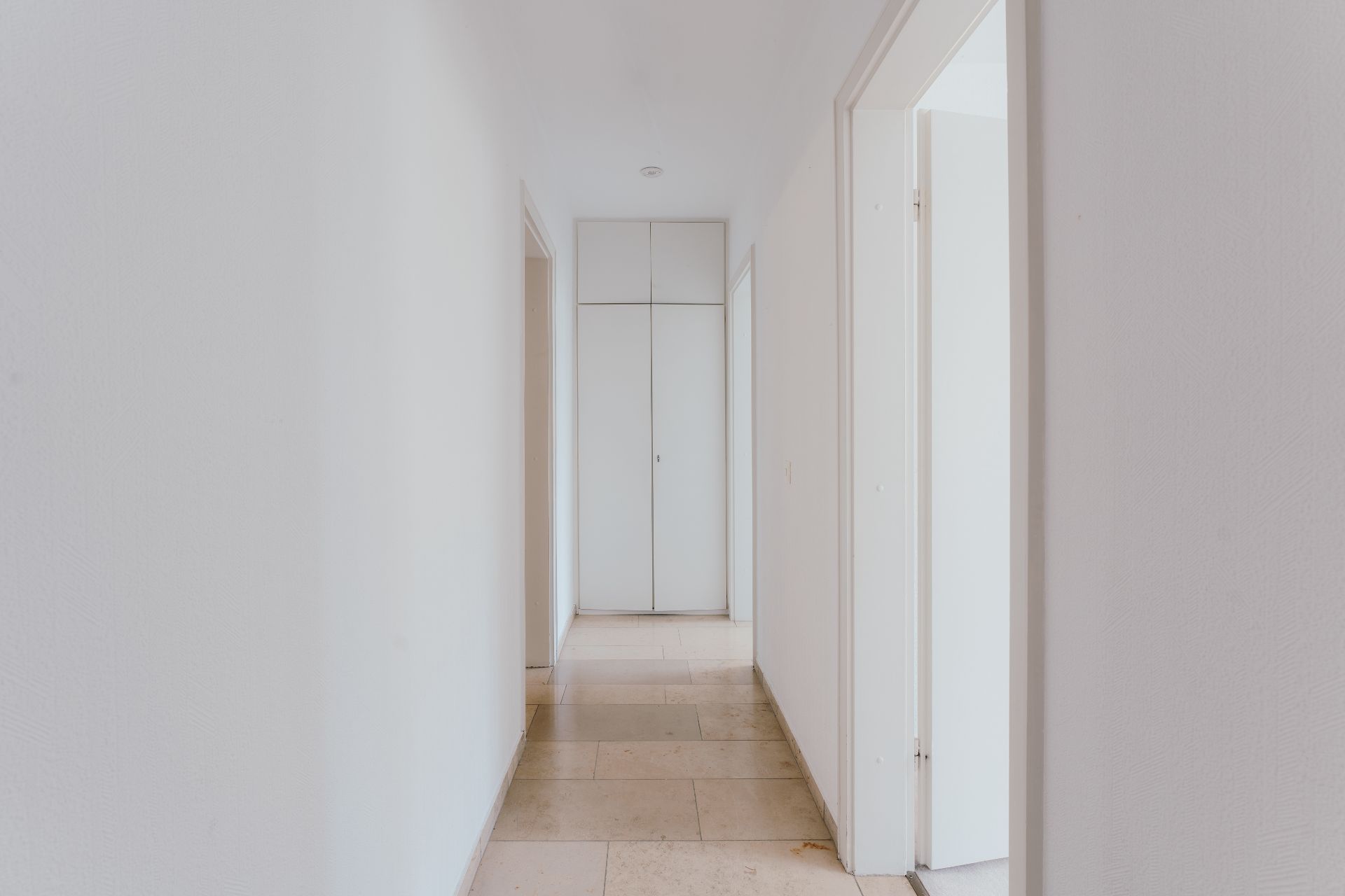 Heller Flur mit weißen Wänden, Türen an den Seiten und Schrank am Ende.