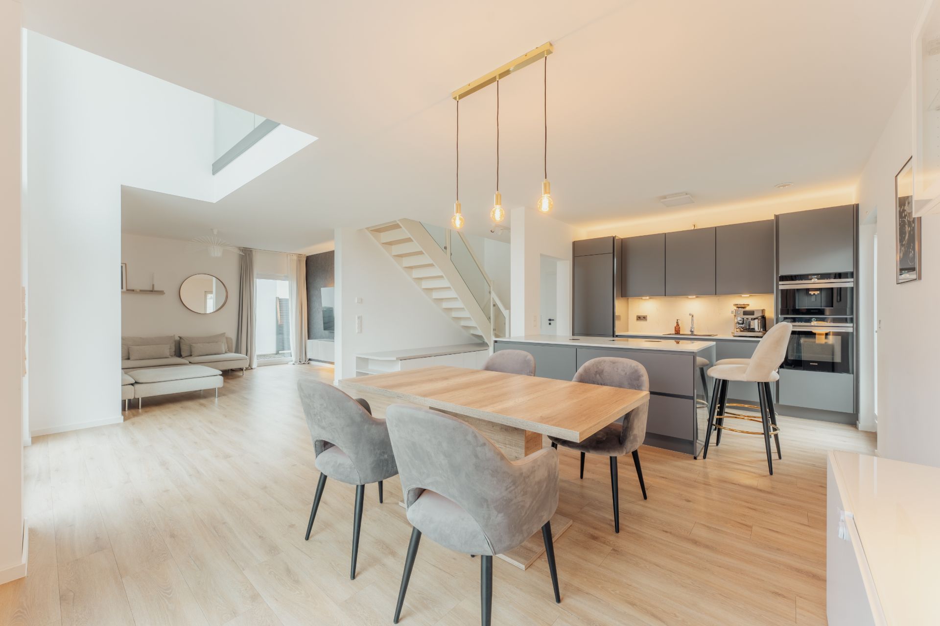 Moderne, offene Wohnküche mit Esstisch, grauen Stühlen und heller Sitzecke.