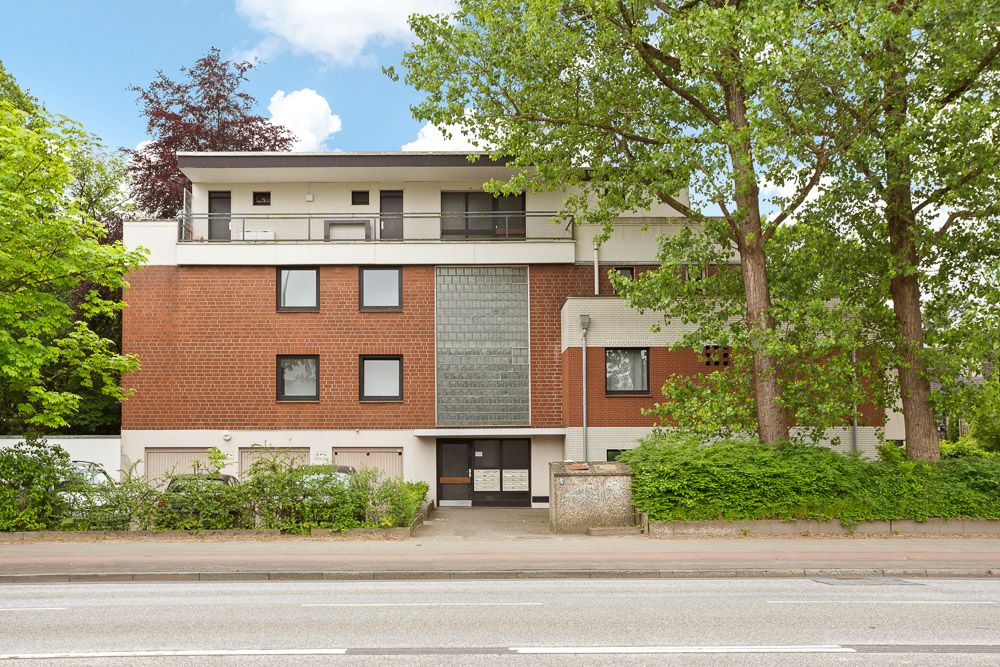 Mehrfamilienhaus mit roter Fassade und Balkon, umgeben von Bäumen und Grünflächen.