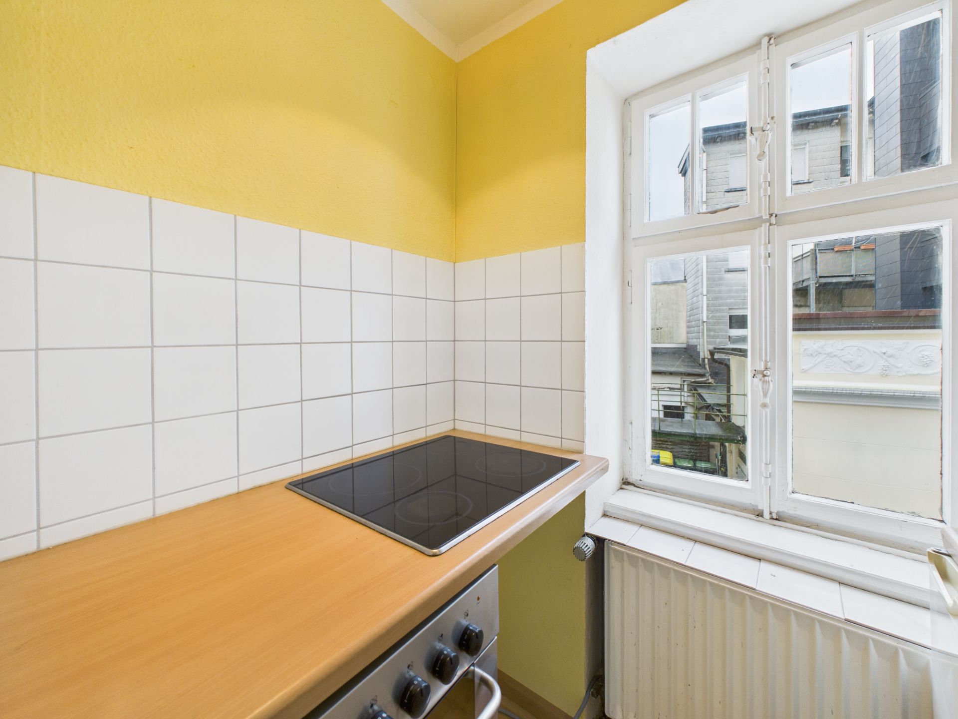 Kleine Küche mit Elektroherd, gelber Wand und Fenster mit Blick nach draußen.
