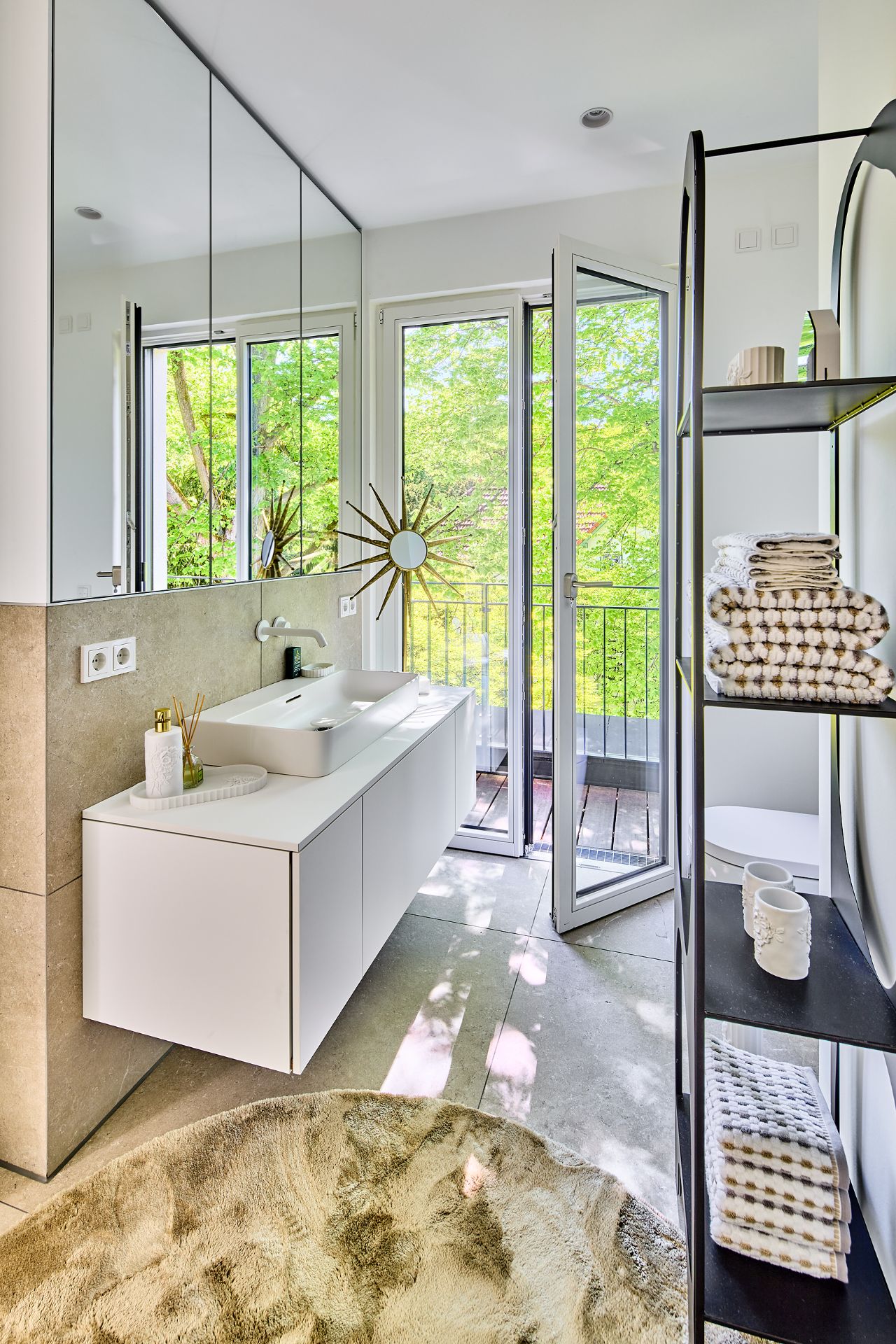 Modernes Badezimmer mit großem Fenster, Waschtisch, Regal mit Handtüchern und offenem Zugang zum Balkon.