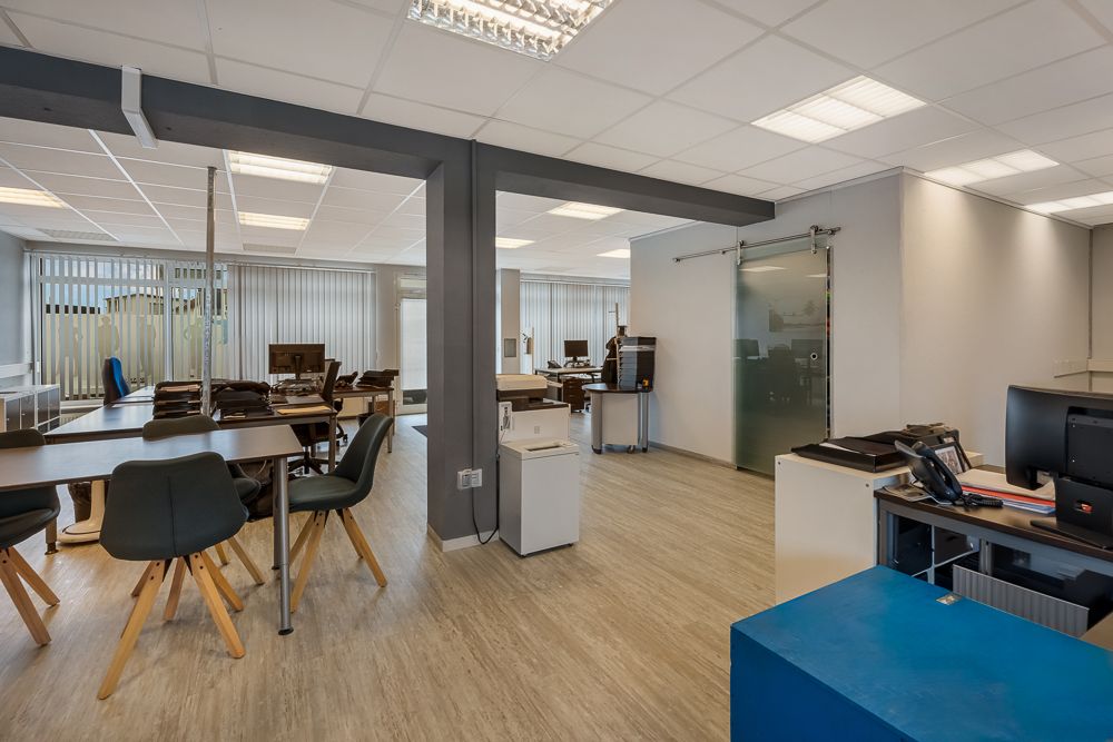 Großer Raum mit Schreibtischen, Stühlen, Computern und großen Fenstern mit Jalousien.