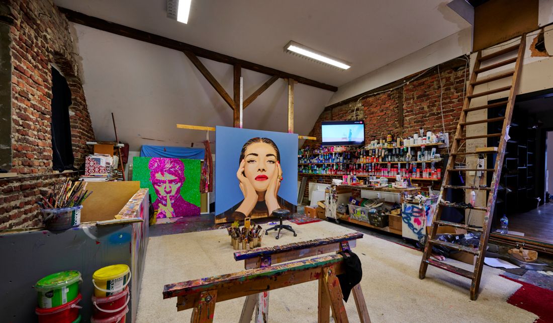 Künstleratelier mit Staffelei, bunten Gemälden, Pinseln und Wandregalen voller Farben.