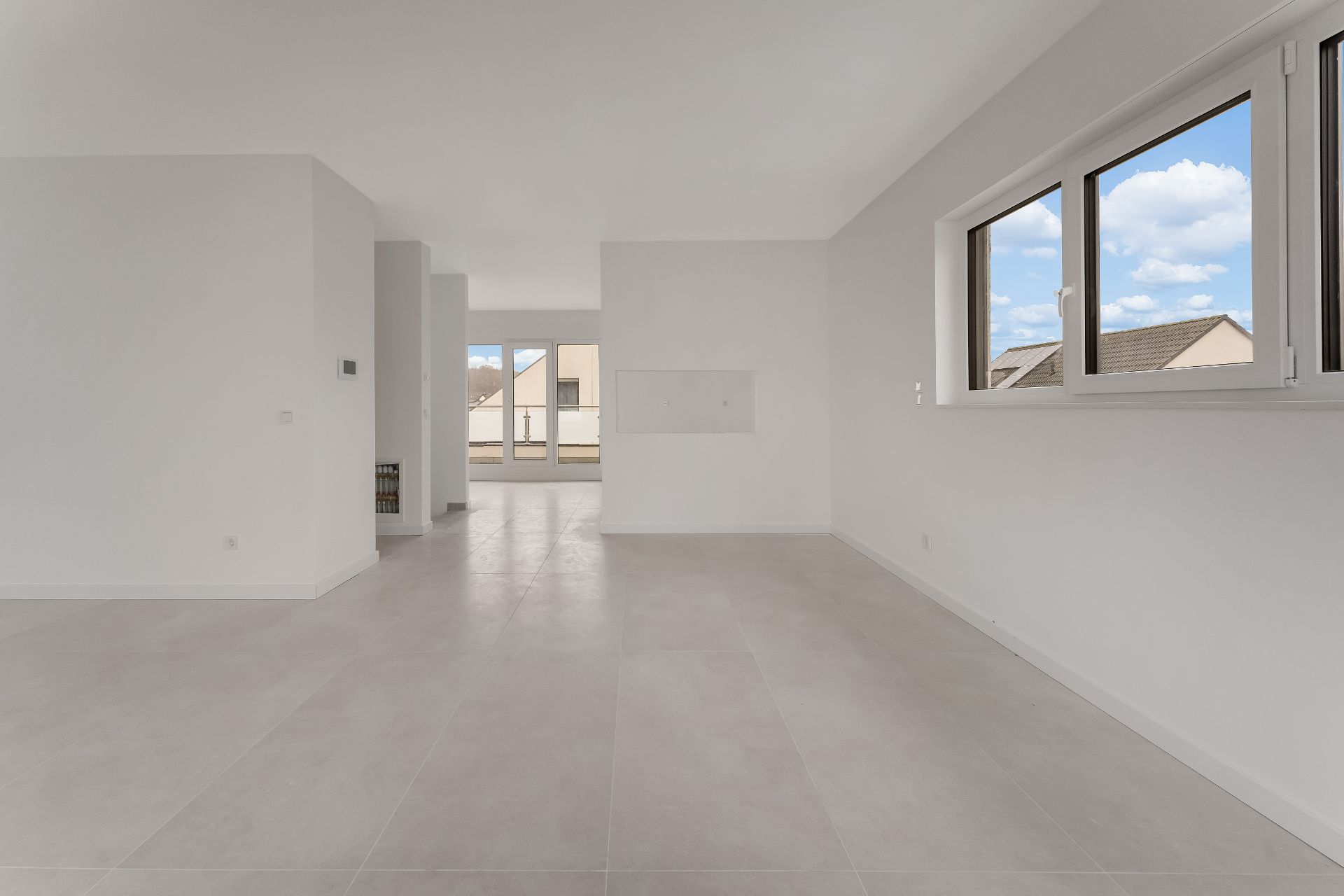 Heller, leerer Raum mit großen Fenstern und Fliesenboden, Blick auf Balkon und Nachbarhäuser.