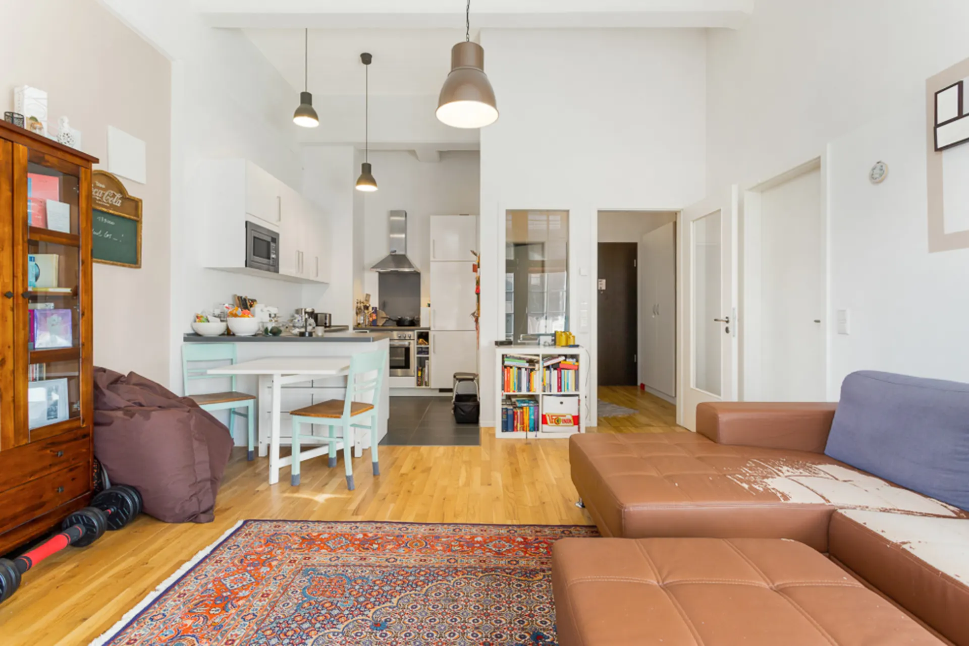 Wohnzimmer mit braunem Sofa, Teppich, offener Küche und Esstisch mit zwei Stühlen.