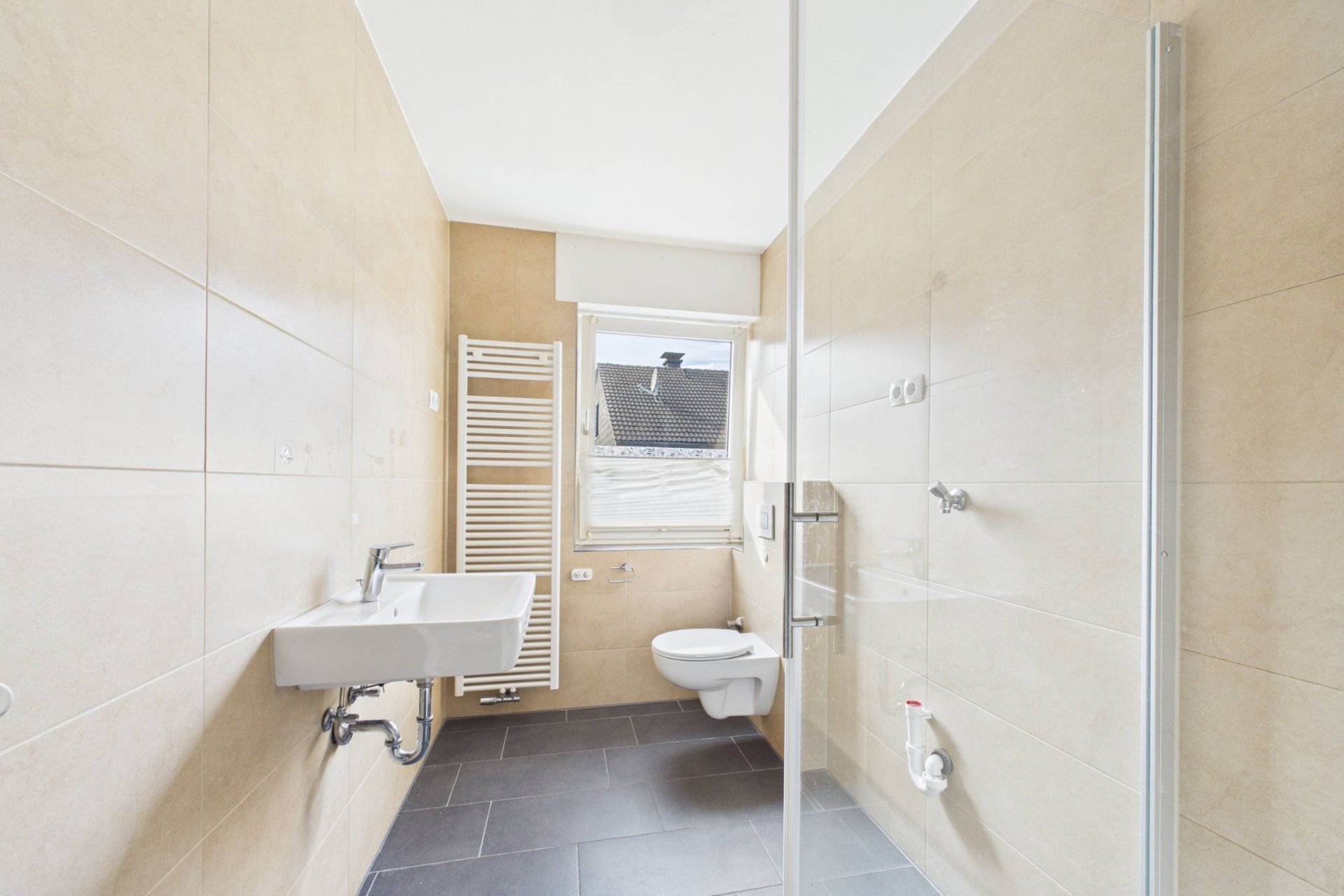 Modernes Bad mit Waschtisch, Toilette, Dusche und Fenster, helle Fliesen.