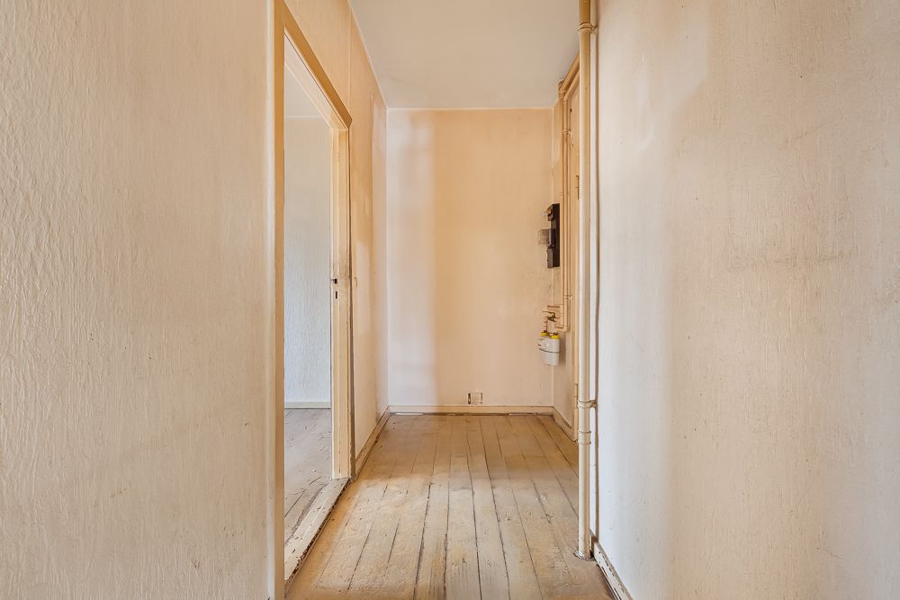 Schmaler Flur mit beigem Wänden und Holzboden, Türen führen zu weiteren Räumen.