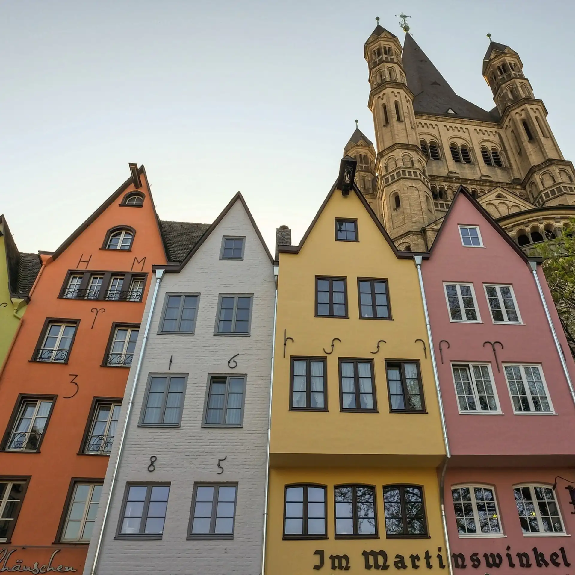 Bunte, schmale Wohnhäuser mit Schrägdächern und großen Fenstern an einer Straße.
