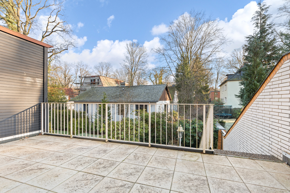 Große Terrasse mit Fliesenboden und Metallgeländer, Ausblick auf Garten und Nachbarhäuser.