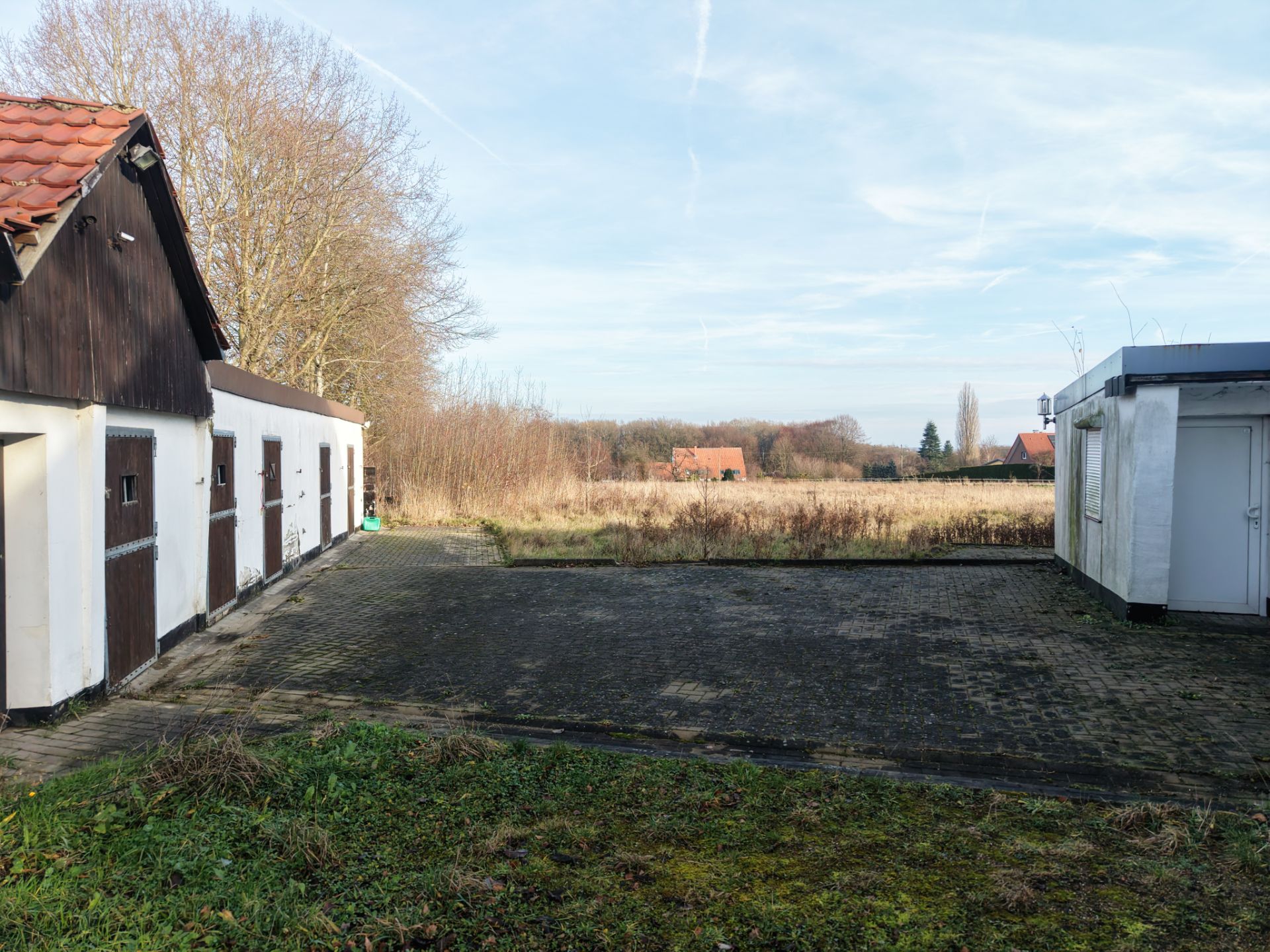 Gepflasterter Hof mit Nebengebäuden und Blick auf Wiese und Bäume im Hintergrund.