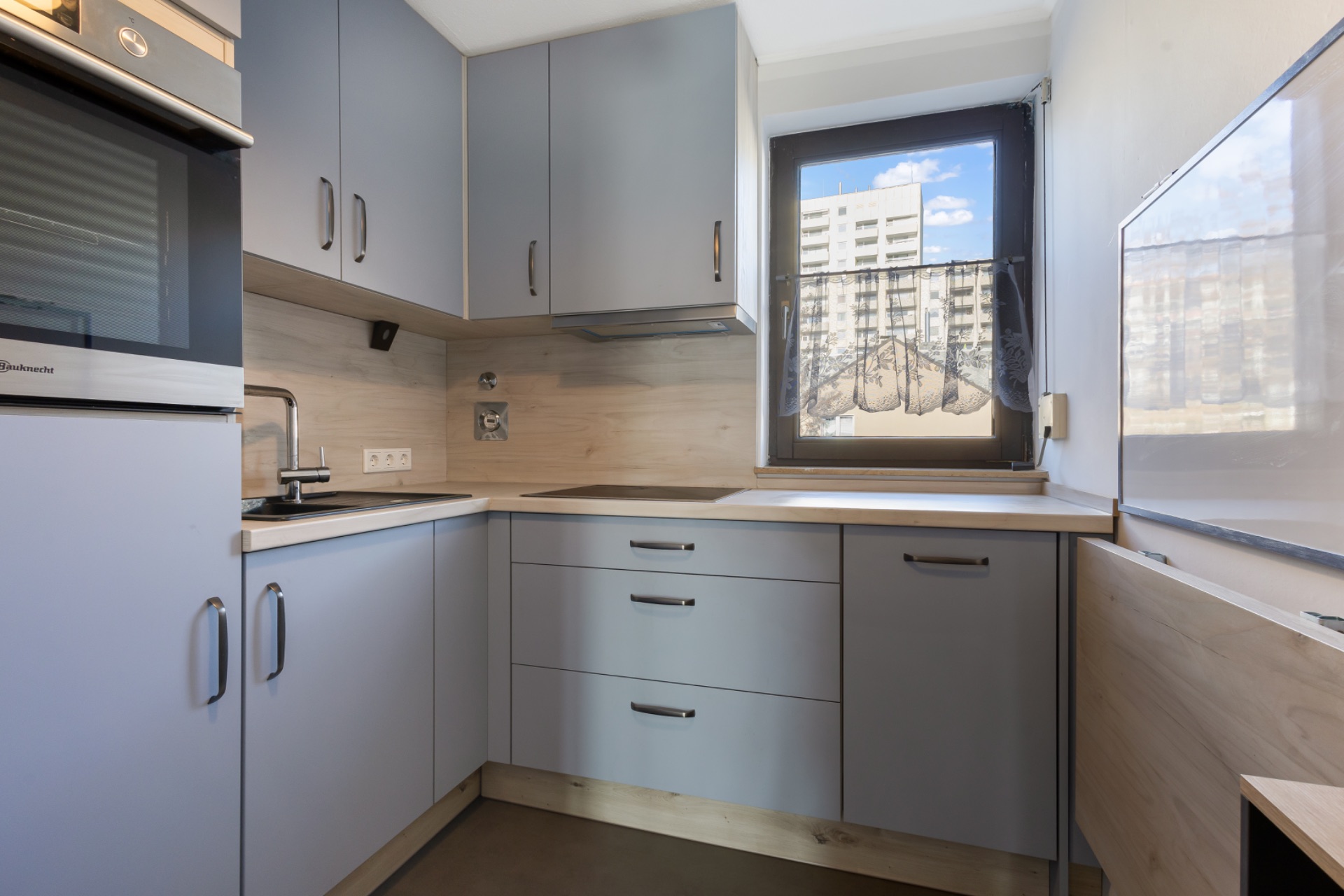 Moderne Küche mit grauen Schränken, Spüle und Fenster mit Blick auf Wohngebäude.