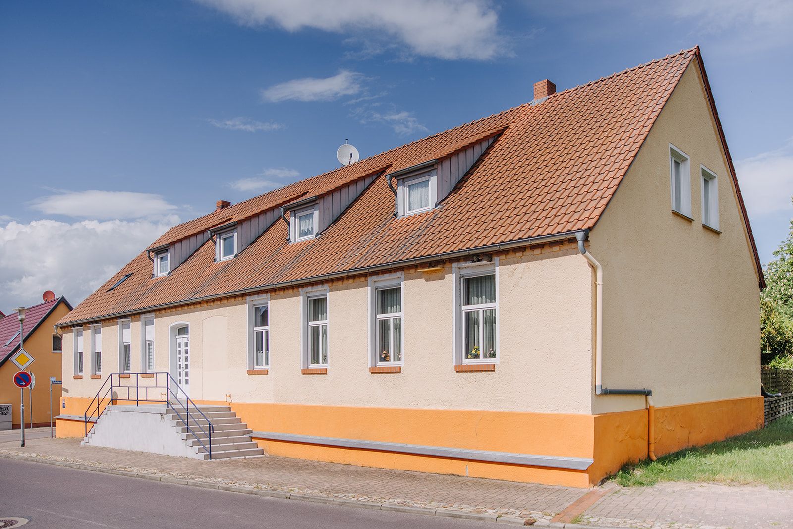Zweistöckiges Wohnhaus mit gelber Fassade, braunem Dach und mehreren Fenstern an der Straße.