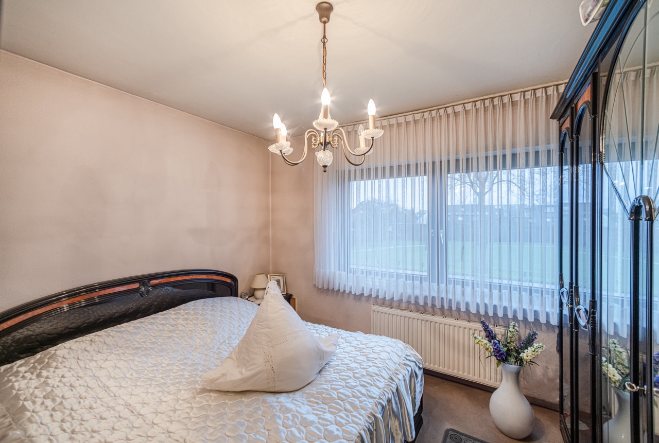Kleines Schlafzimmer mit Doppelbett, Kronleuchter und großem Fenster mit Gardinen.