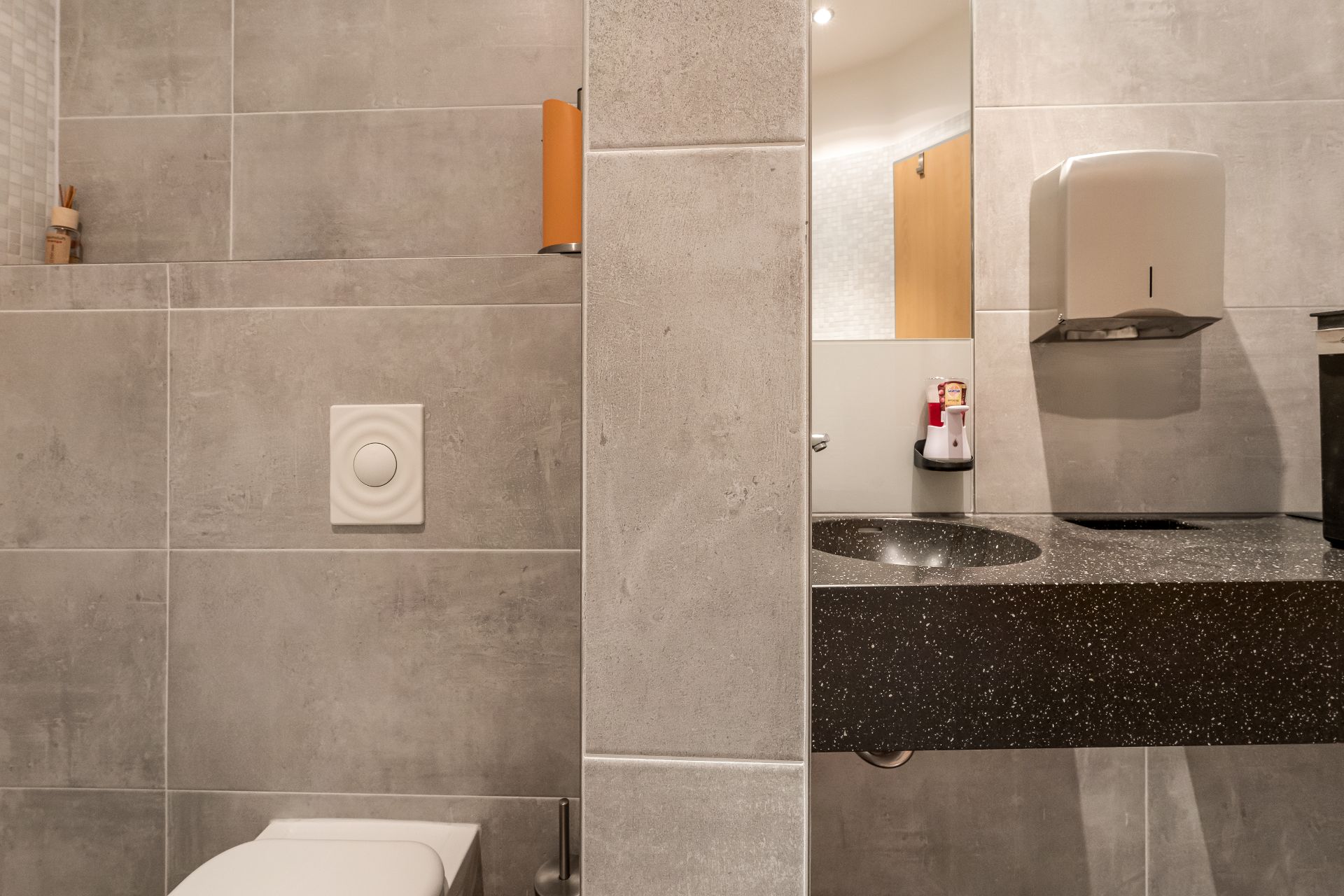 Modernes Badezimmer mit grauen Fliesen, Toilette und Waschbecken mit Spiegel.