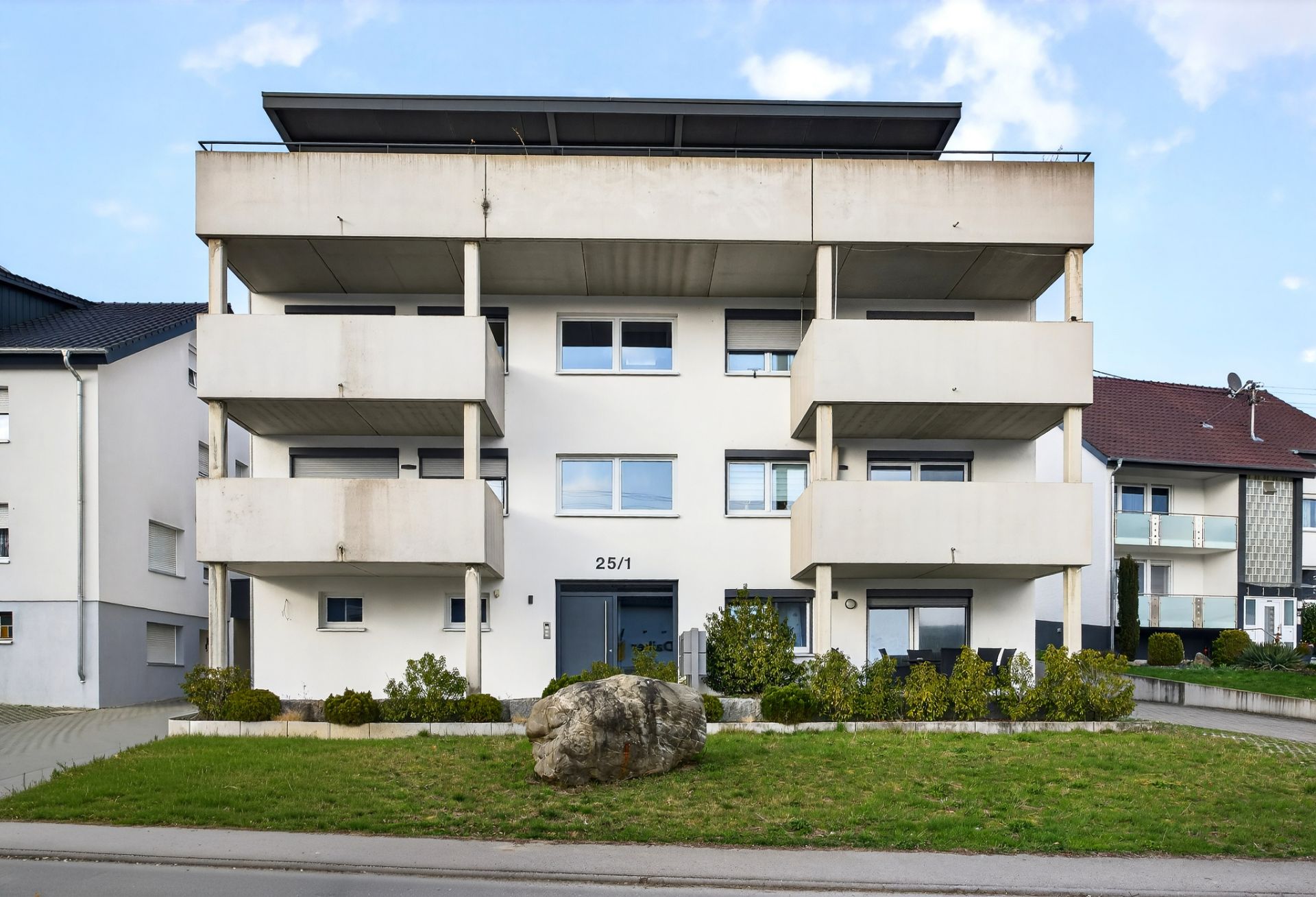 Modernes dreistöckiges Wohnhaus mit Balkonen und grünem Vorgarten.