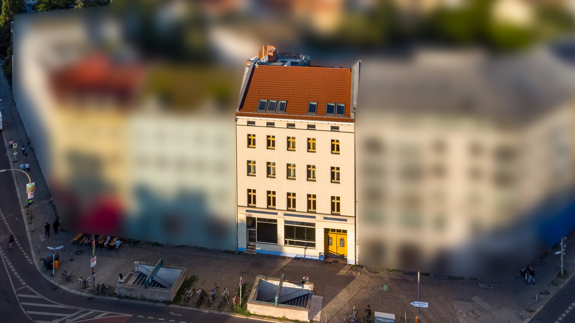 Mehrstöckiges Wohnhaus mit hellgelber Fassade und rotem Dach an einer Straßenecke.