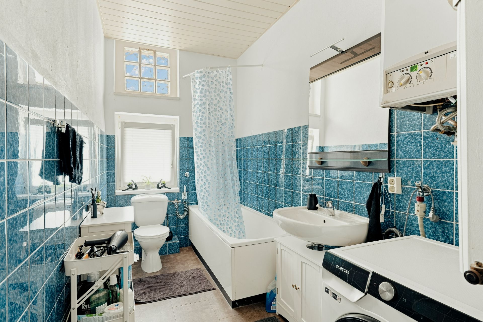 Helles Badezimmer mit blauen Fliesen, Badewanne, Waschbecken, Toilette und Waschmaschine.