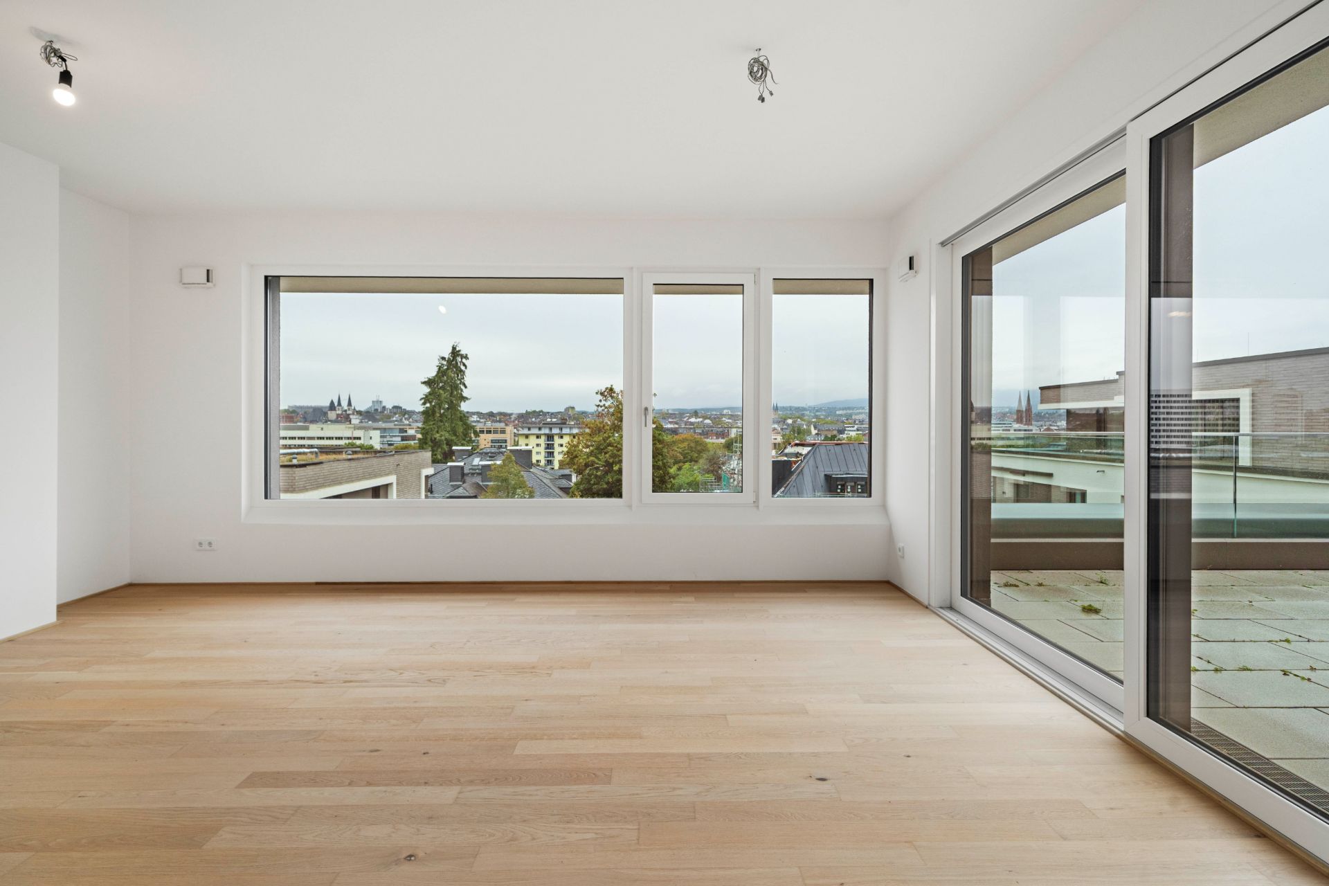 Helles Wohnzimmer mit großen Fenstern und Holzfußboden, Blick auf die Stadt.