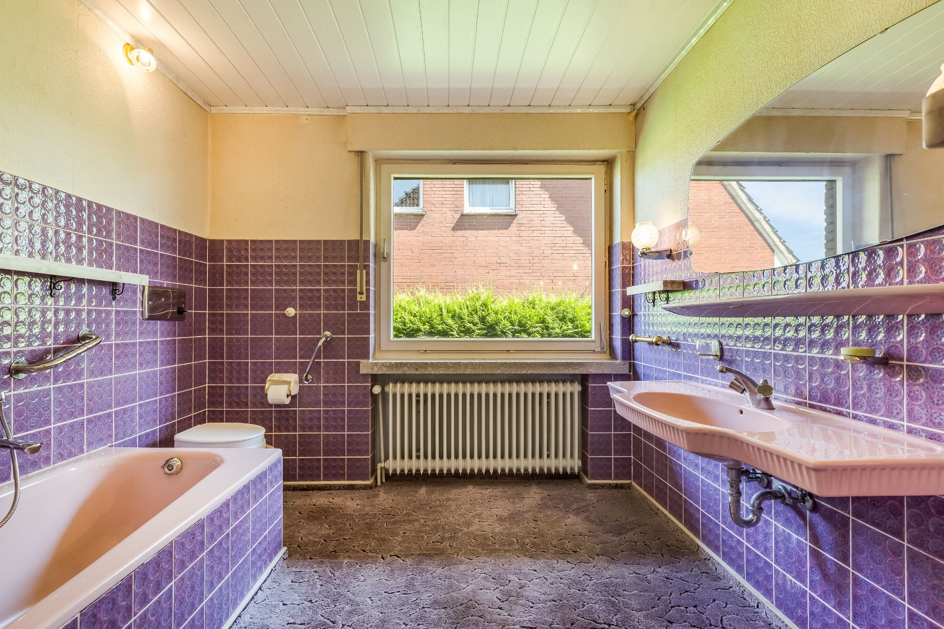 Badezimmer mit lila Fliesen, Badewanne, Waschbecken, Toilette und großem Fenster.