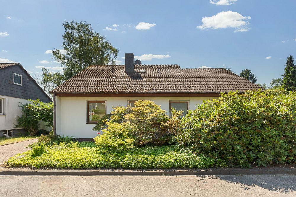 Einfamilienhaus mit Satteldach und großem Vorgarten mit Sträuchern und Büschen.