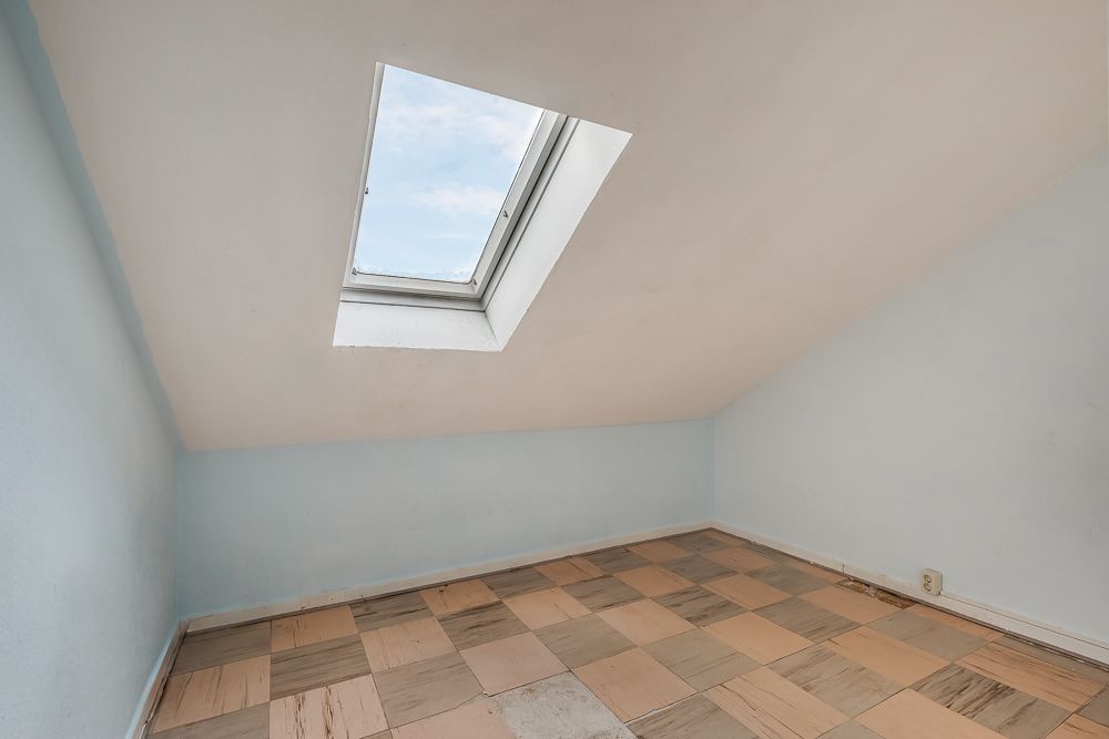 Kleines Zimmer mit Schrägdach, Dachfenster und gefliestem Boden.