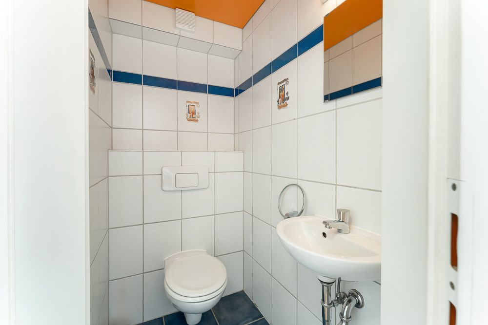 Kleines WC mit weiß gefliesten Wänden, Wandtoilette, Waschbecken und Spiegel.