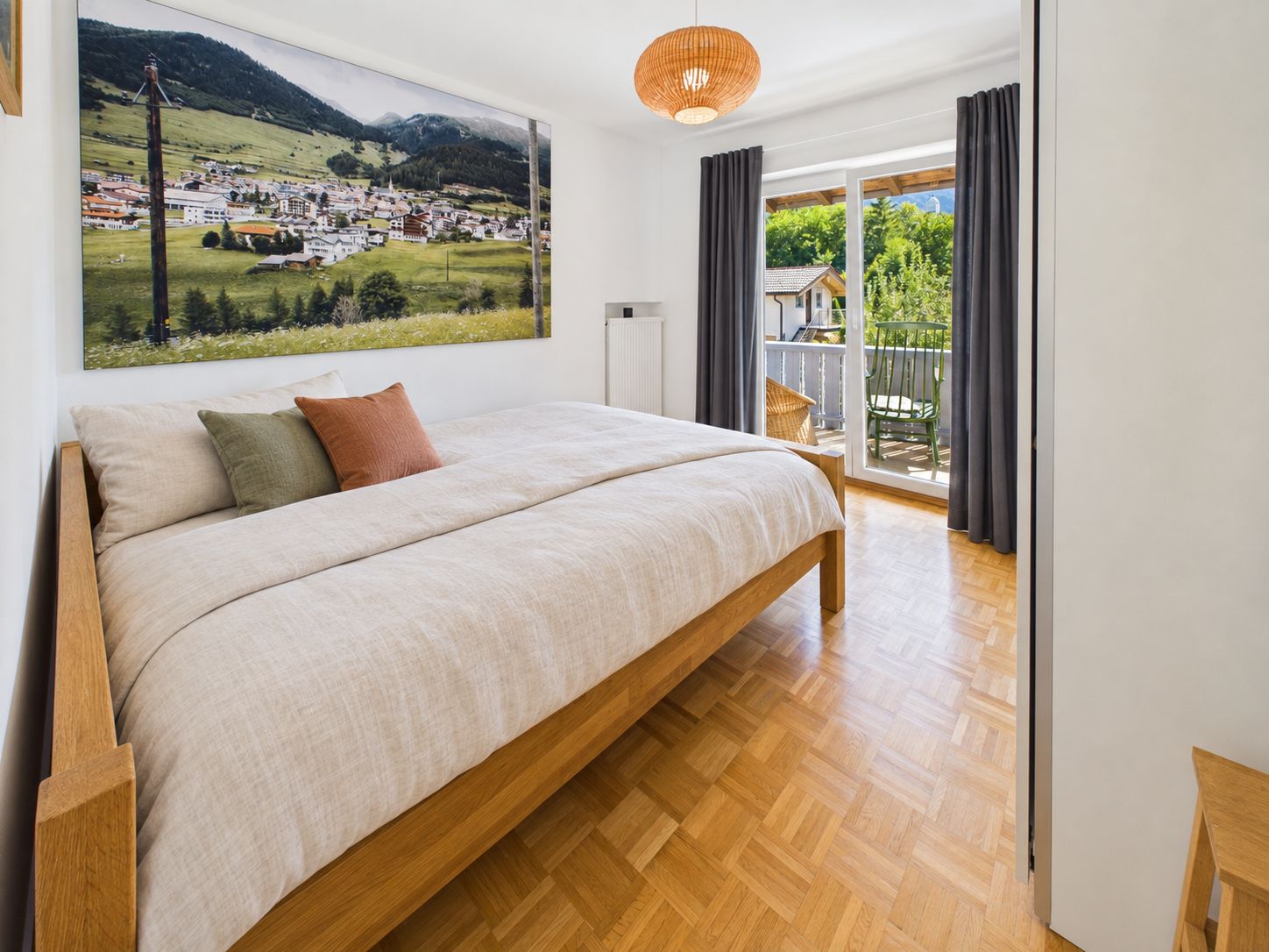 Helles Schlafzimmer mit großem Bett, Holzboden, Wandbild und Zugang zu einem Balkon mit Sitzmöbeln.
