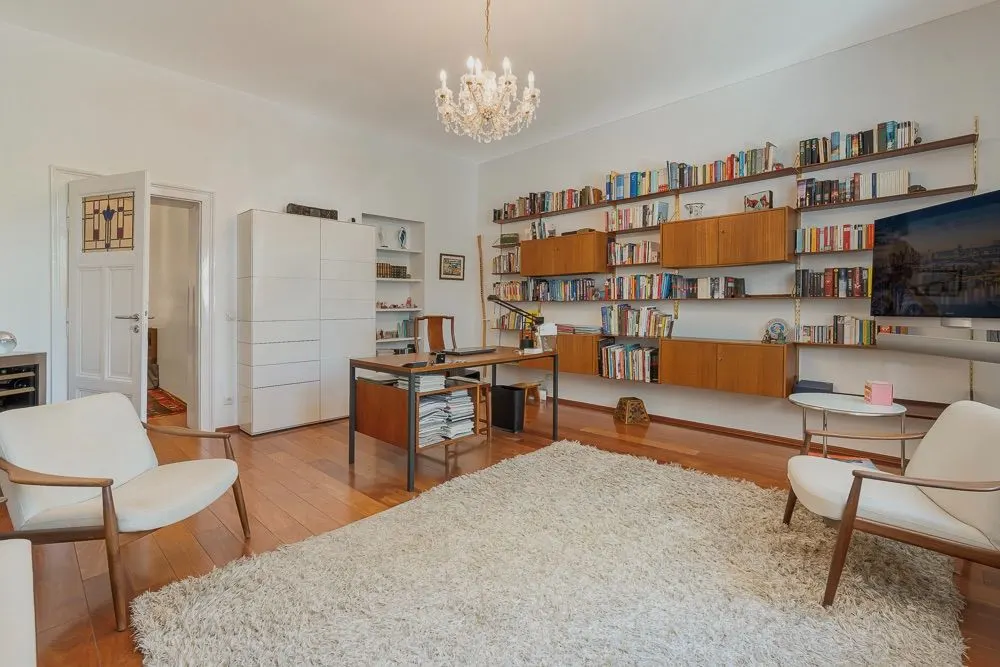Helles Arbeitszimmer mit Schreibtisch, Bücherregalen, Sesseln und Teppich auf Holzfußboden.