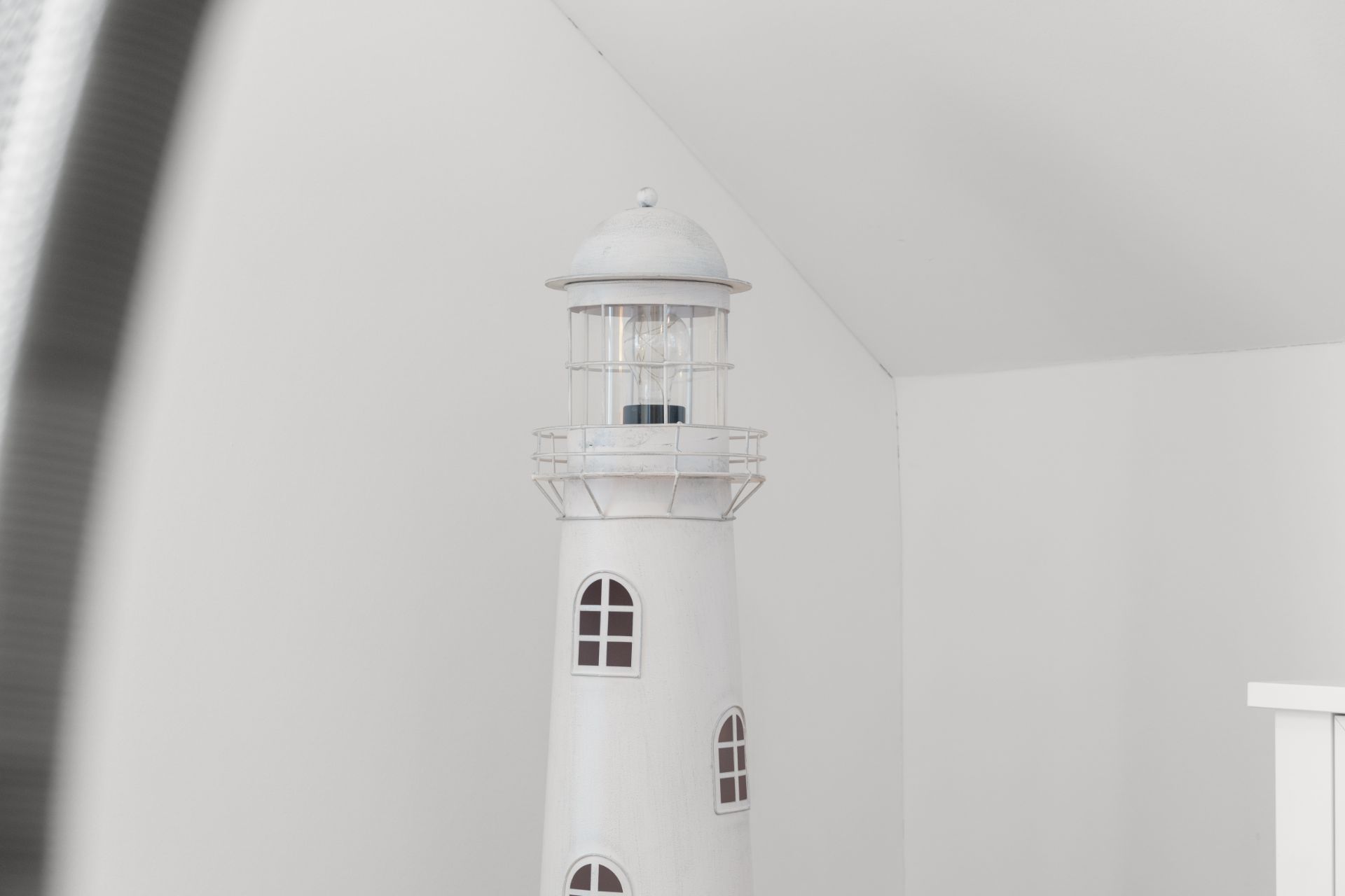 Weiße Deko-Leuchtturmfigur steht in einer hellen Zimmerecke.
