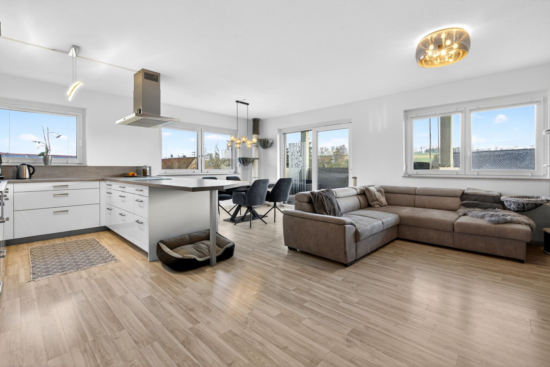 Helles Wohnzimmer mit offener Küche, Esstisch, großer Ecksofa und Holzboden.