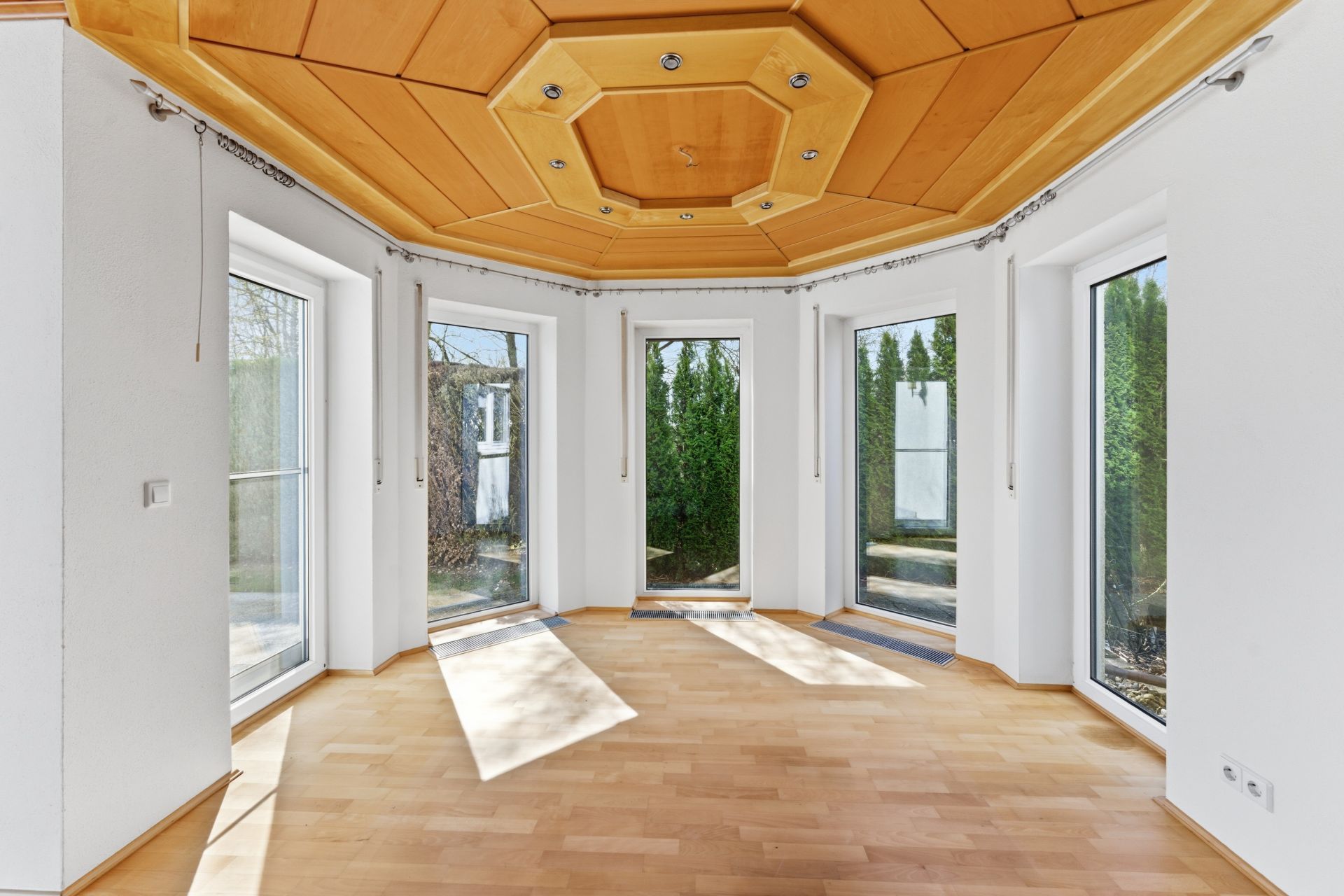 Heller Raum mit Holzdecke, großen Fenstern und Parkettboden.