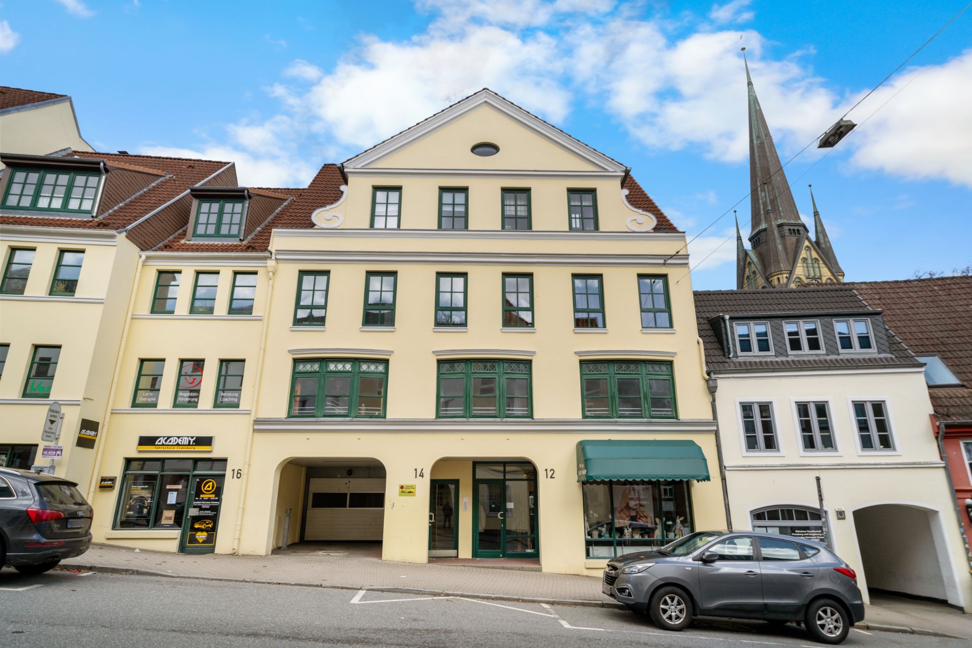 Mehrstöckiges Wohnhaus mit grünen Fenstern und Geschäften im Erdgeschoss an einer Straße.