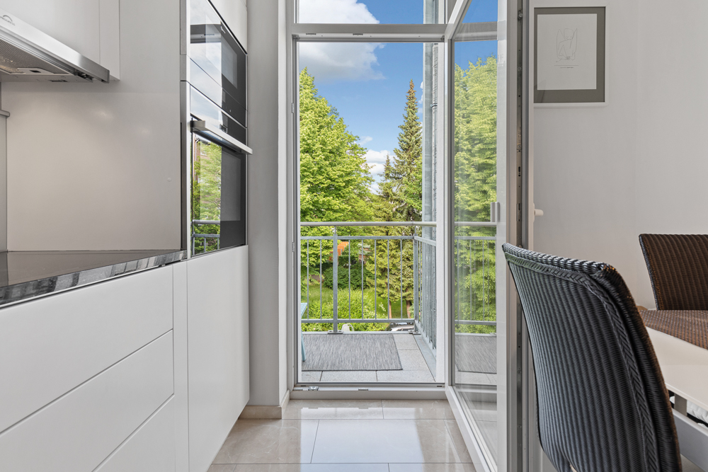 Moderne Küche mit offenem Zugang zu einem Balkon mit Blick auf grüne Bäume.