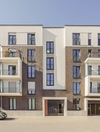 Modernes Wohngebäude mit Balkonen, großen Fenstern und geparkten Autos davor.