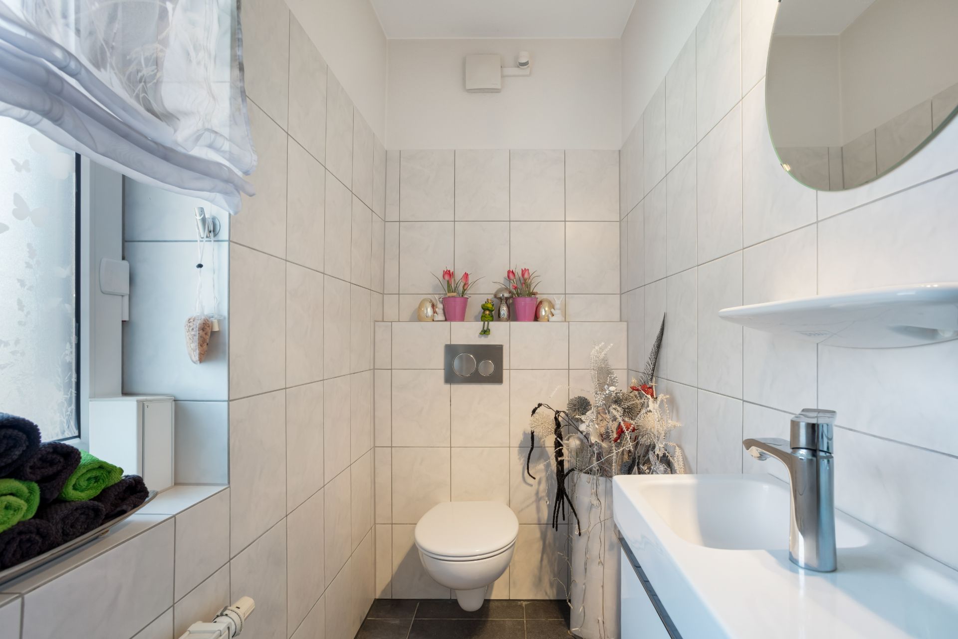 Kleines, modernes Badezimmer mit Wandtoilette, Waschbecken und Dekorationen auf Fliesen.