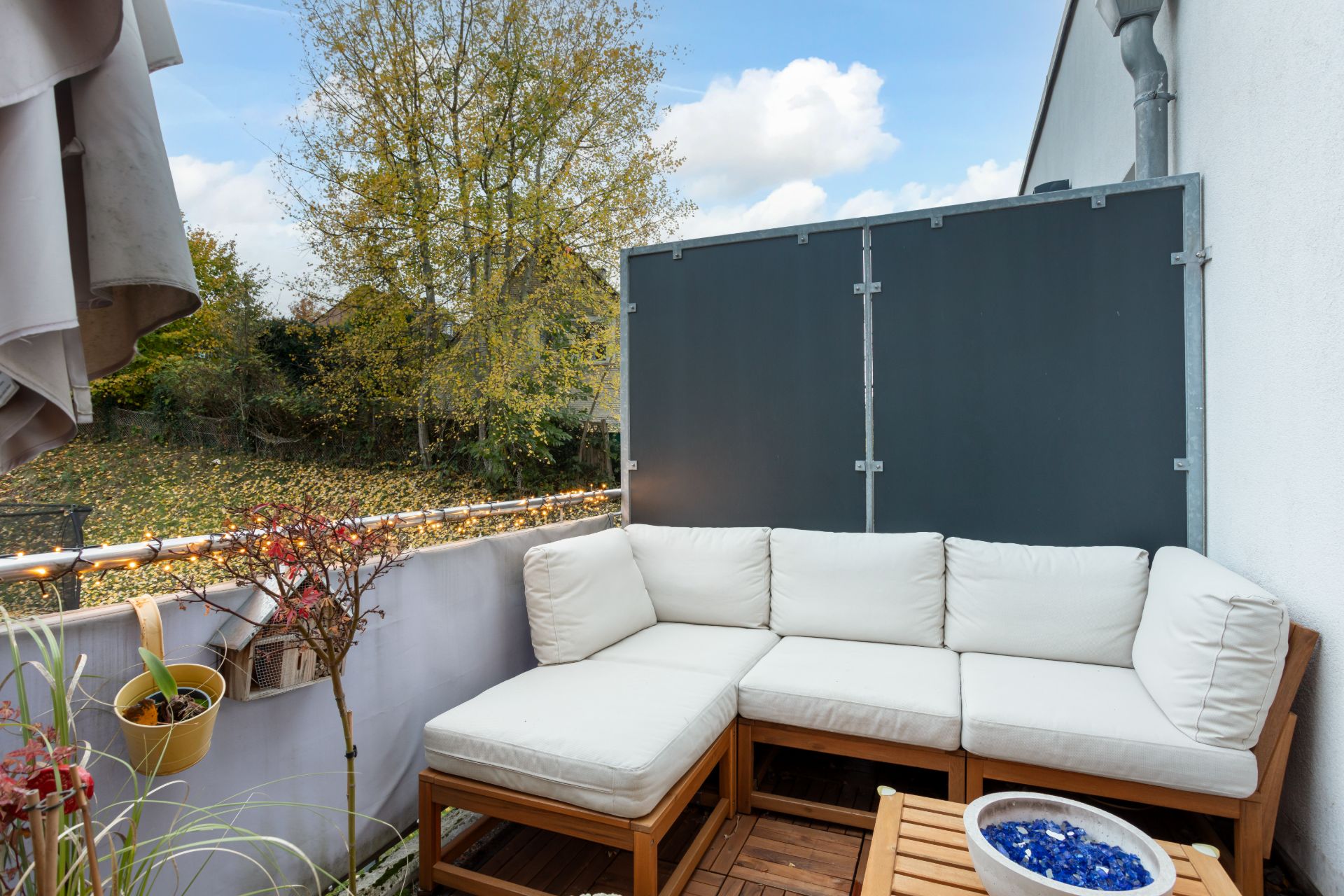 Kleine Terrasse mit weißer Eckcouch, Pflanzen und Tisch im Freien.