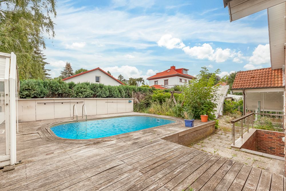 Garten mit rundem Pool, Holzterrasse und einigen Pflanzen in Töpfen.