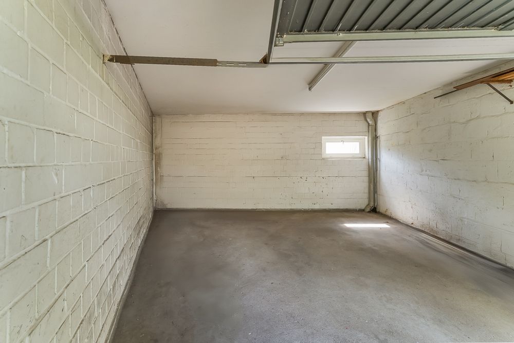 Leere Garage mit weiß gestrichenen Wänden, Betonboden und kleinem Fenster an der Rückwand.