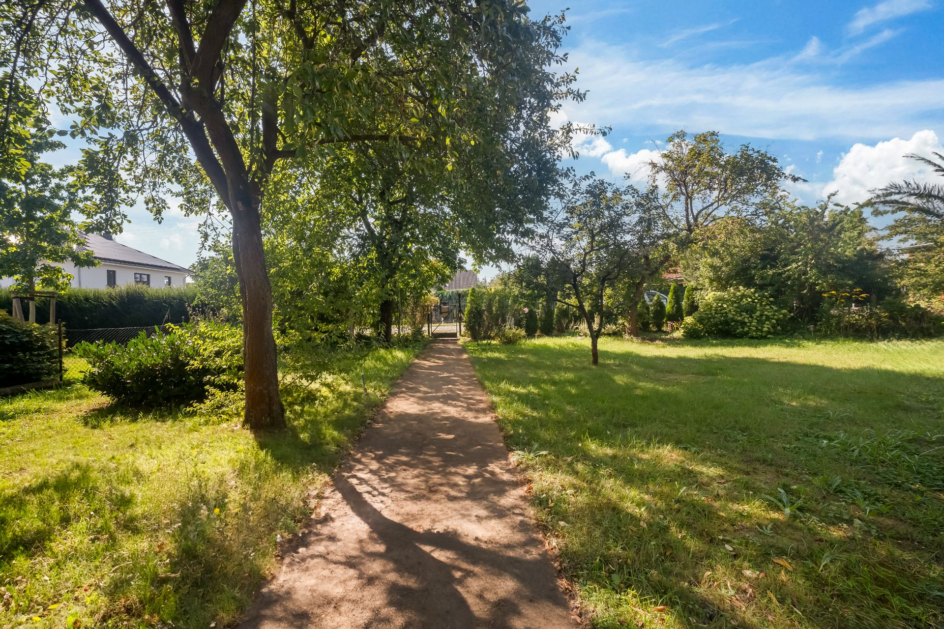 Gepflasterter Weg führt durch einen grünen Garten mit Bäumen und Sträuchern.